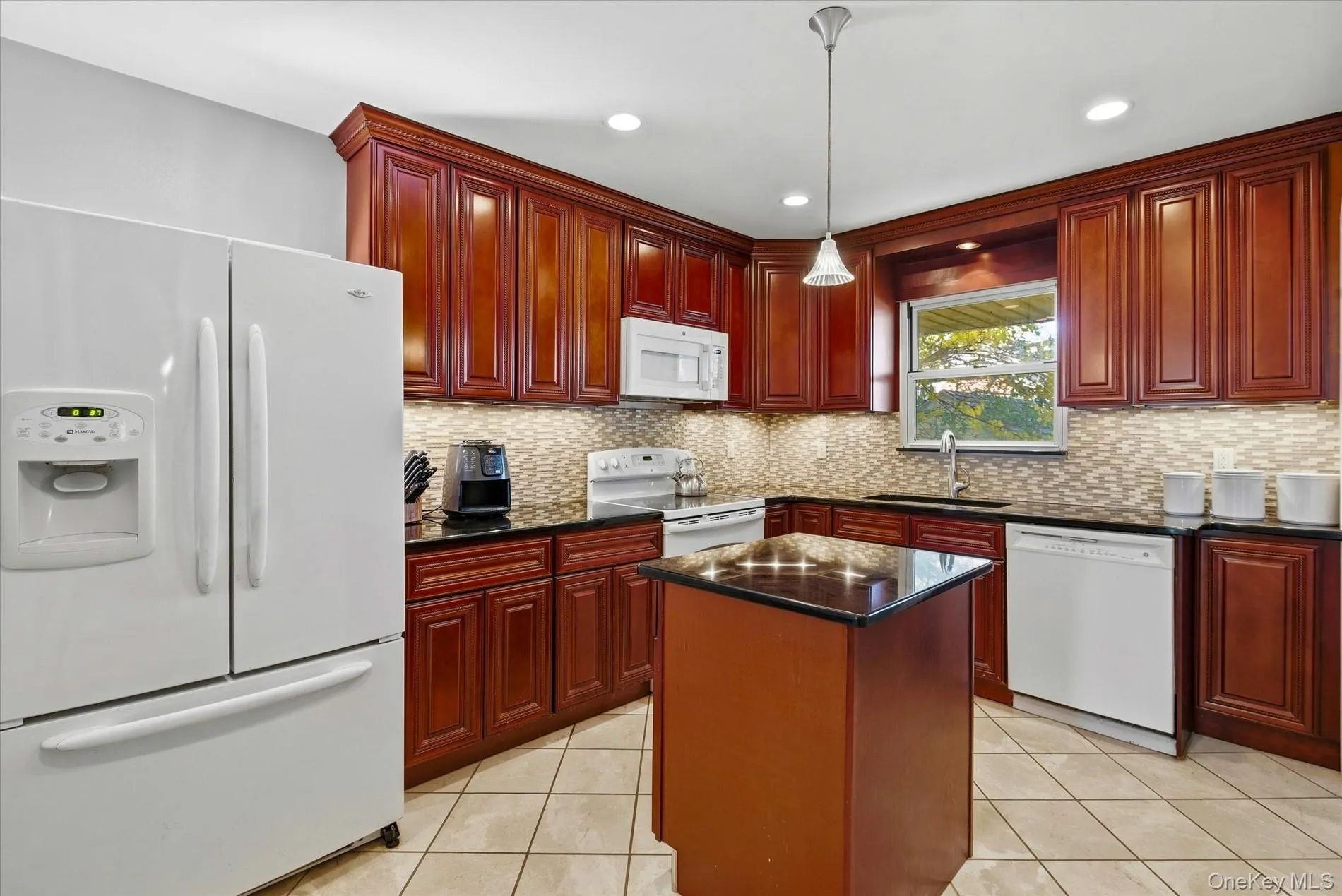 Kitchen with white appliances, reddish brown cabinets, light tile patterned flooring, hanging light fixtures, and recessed lighting Kitchen with white appliances, reddish brown cabinets, light tile patterned flooring, hanging light fixtures, and recessed lighting