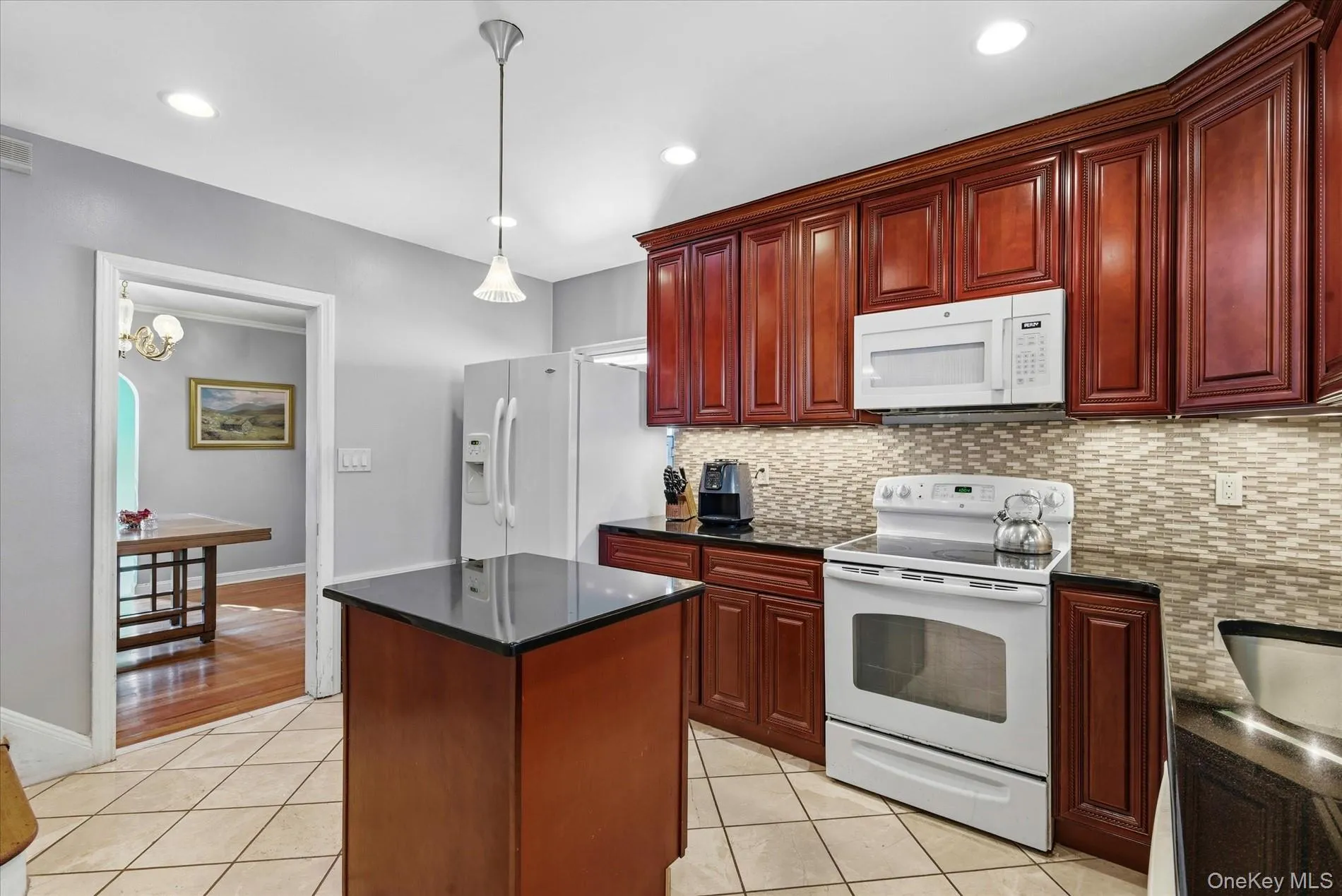 Kitchen with white appliances, decorative backsplash, dark brown cabinets, light tile patterned flooring, and decorative light fixtures Kitchen with white appliances, decorative backsplash, dark brown cabinets, light tile patterned flooring, and decorative light fixtures