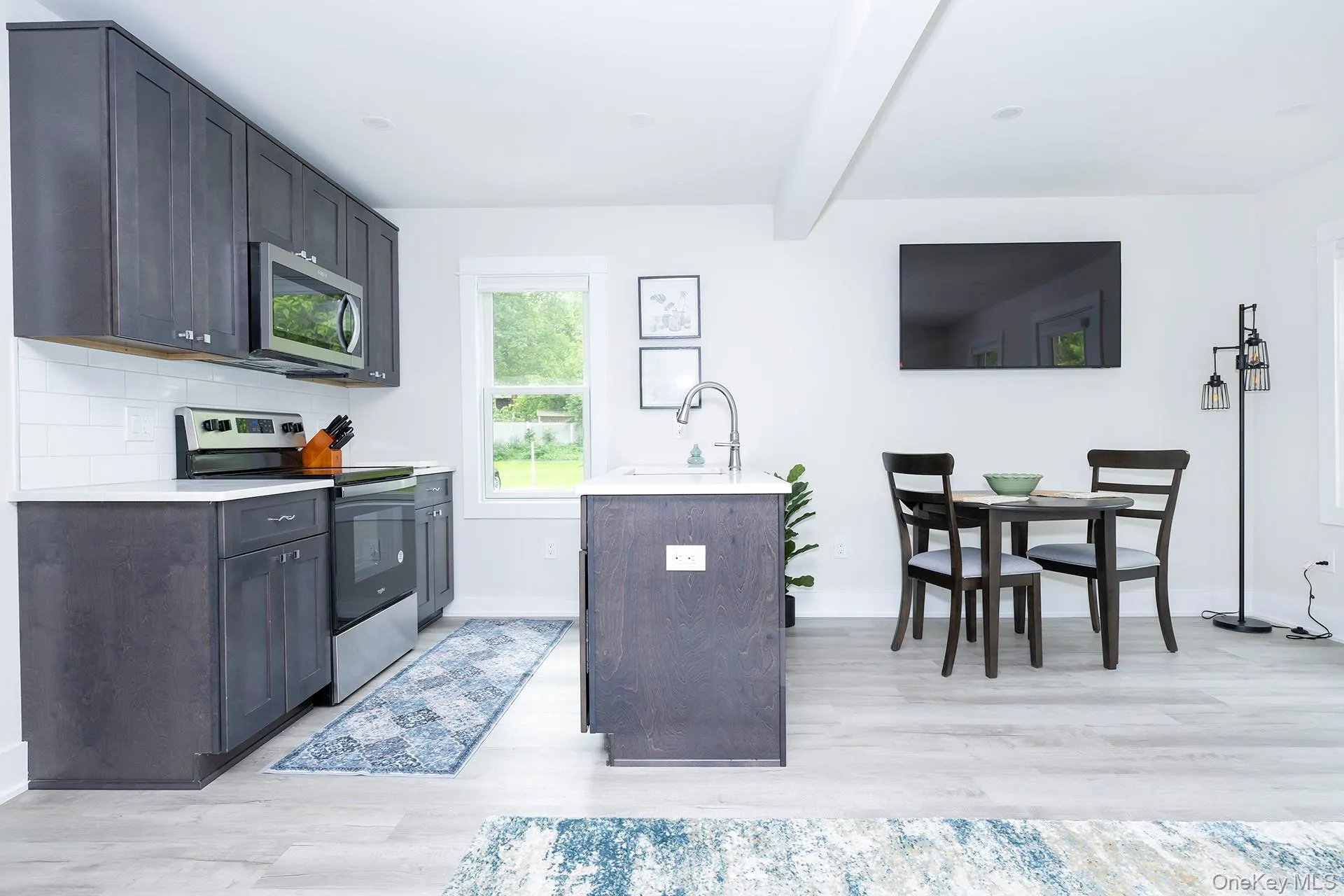 Kitchen with stainless steel appliances, beamed ceiling, light wood-style flooring, and backsplash Kitchen with stainless steel appliances, beamed ceiling, light wood-style flooring, and backsplash