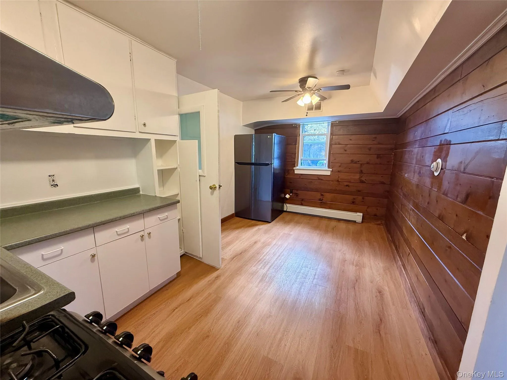 Kitchen with white cabinetry, freestanding refrigerator, light wood-type flooring, and wood walls Kitchen with white cabinetry, freestanding refrigerator, light wood-type flooring, and wood walls
