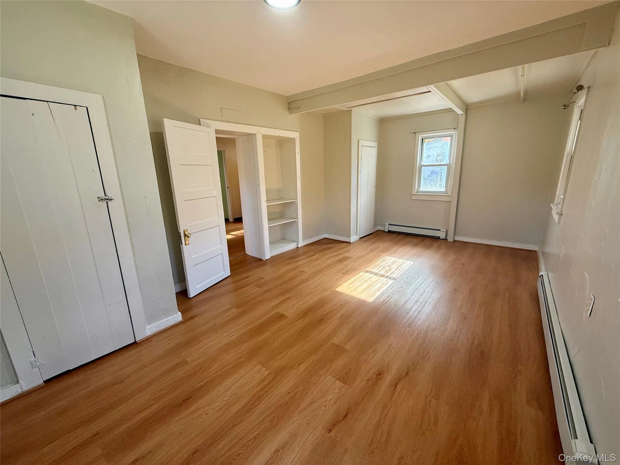 Unfurnished bedroom with a baseboard radiator, light wood-type flooring, and beam ceiling Unfurnished bedroom with a baseboard radiator, light wood-type flooring, and beam ceiling