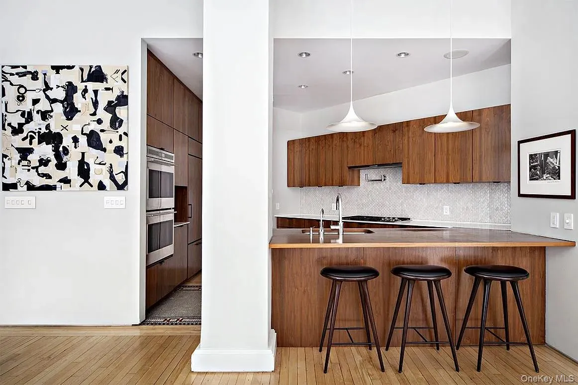 Kitchen with brown cabinets, modern cabinets, hanging light fixtures, a kitchen breakfast bar, and light wood-style flooring Kitchen with brown cabinets, modern cabinets, hanging light fixtures, a kitchen breakfast bar, and light wood-style flooring