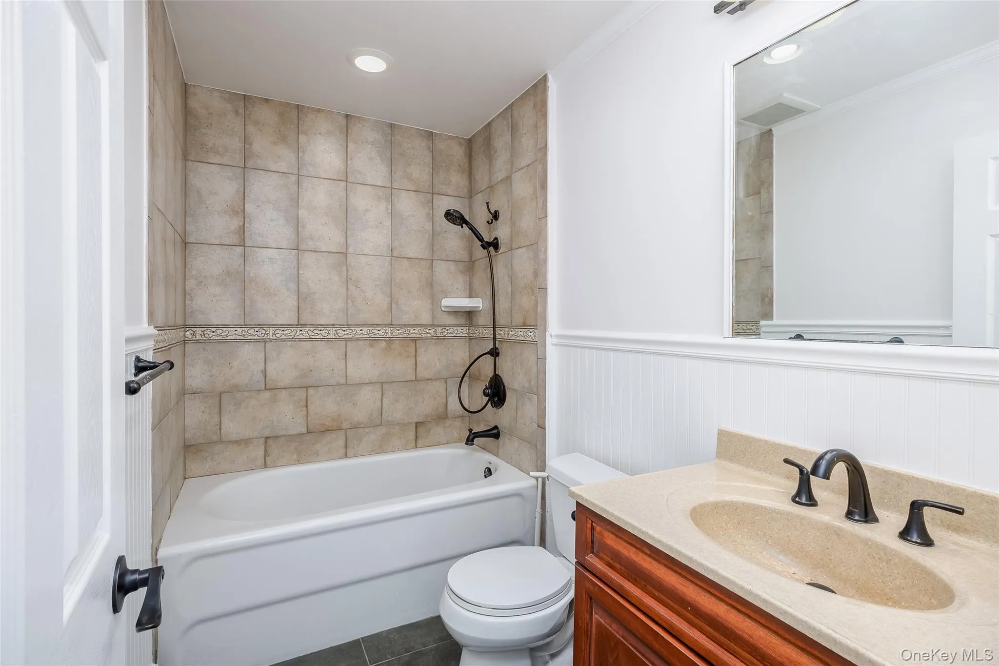 Bathroom with vanity, bathing tub / shower combination, dark tile patterned floors, a wainscoted wall, and recessed lighting Bathroom with vanity, bathing tub / shower combination, dark tile patterned floors, a wainscoted wall, and recessed lighting