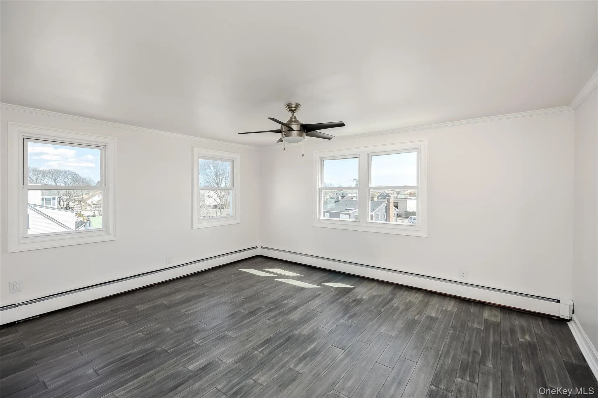 Empty room featuring a baseboard heating unit, ornamental molding, dark wood-style floors, and a ceiling fan Empty room featuring a baseboard heating unit, ornamental molding, dark wood-style floors, and a ceiling fan