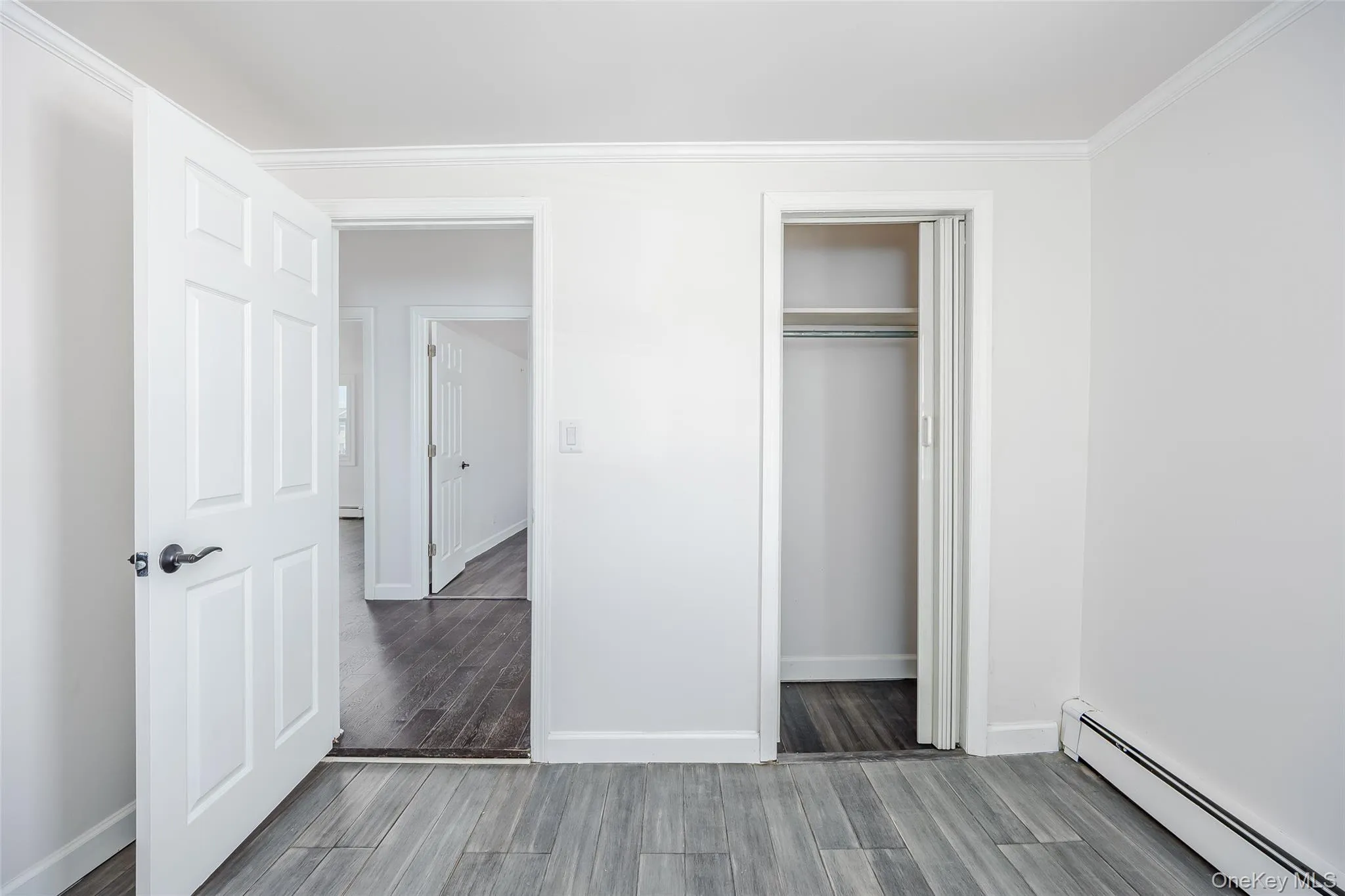 Unfurnished bedroom featuring a baseboard heating unit, wood finished floors, a closet, and ornamental molding Unfurnished bedroom featuring a baseboard heating unit, wood finished floors, a closet, and ornamental molding