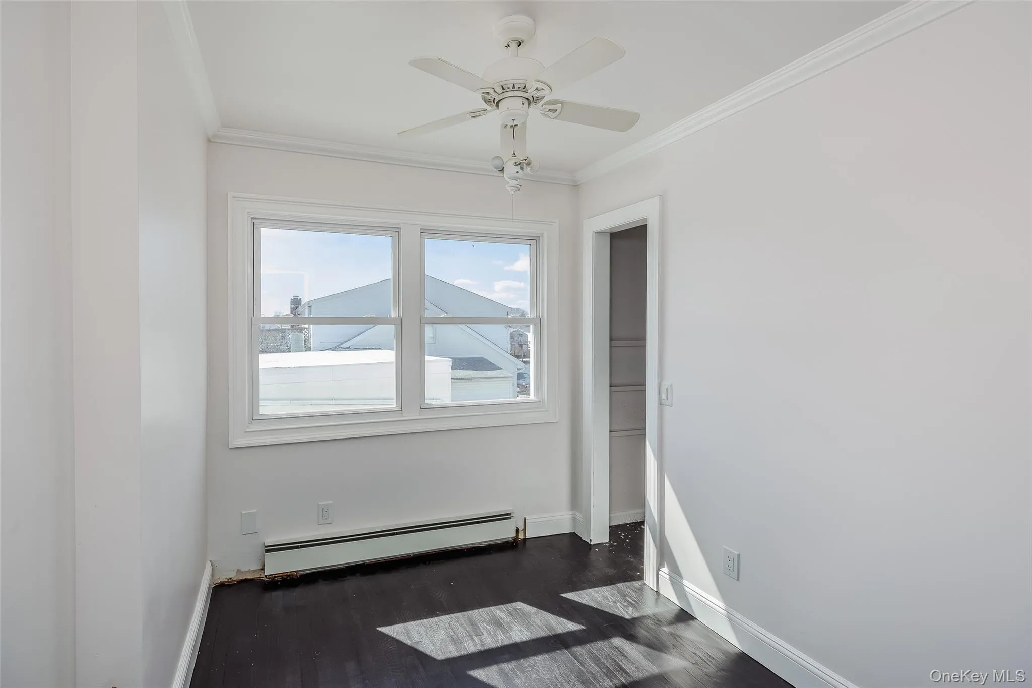 Empty room featuring a baseboard heating unit, crown molding, dark wood-style floors, and ceiling fan Empty room featuring a baseboard heating unit, crown molding, dark wood-style floors, and ceiling fan
