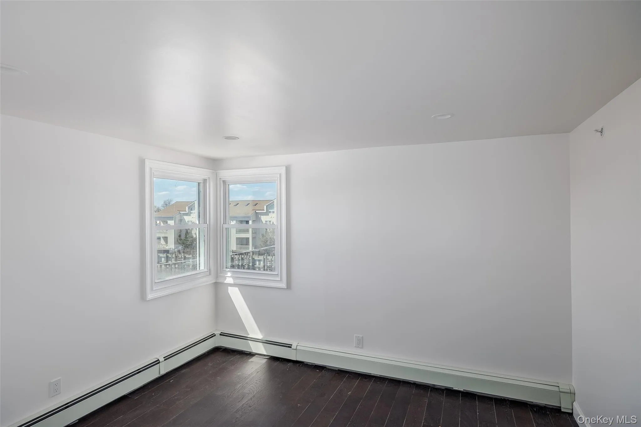 Empty room featuring dark wood-style flooring and a baseboard heating unit Empty room featuring dark wood-style flooring and a baseboard heating unit