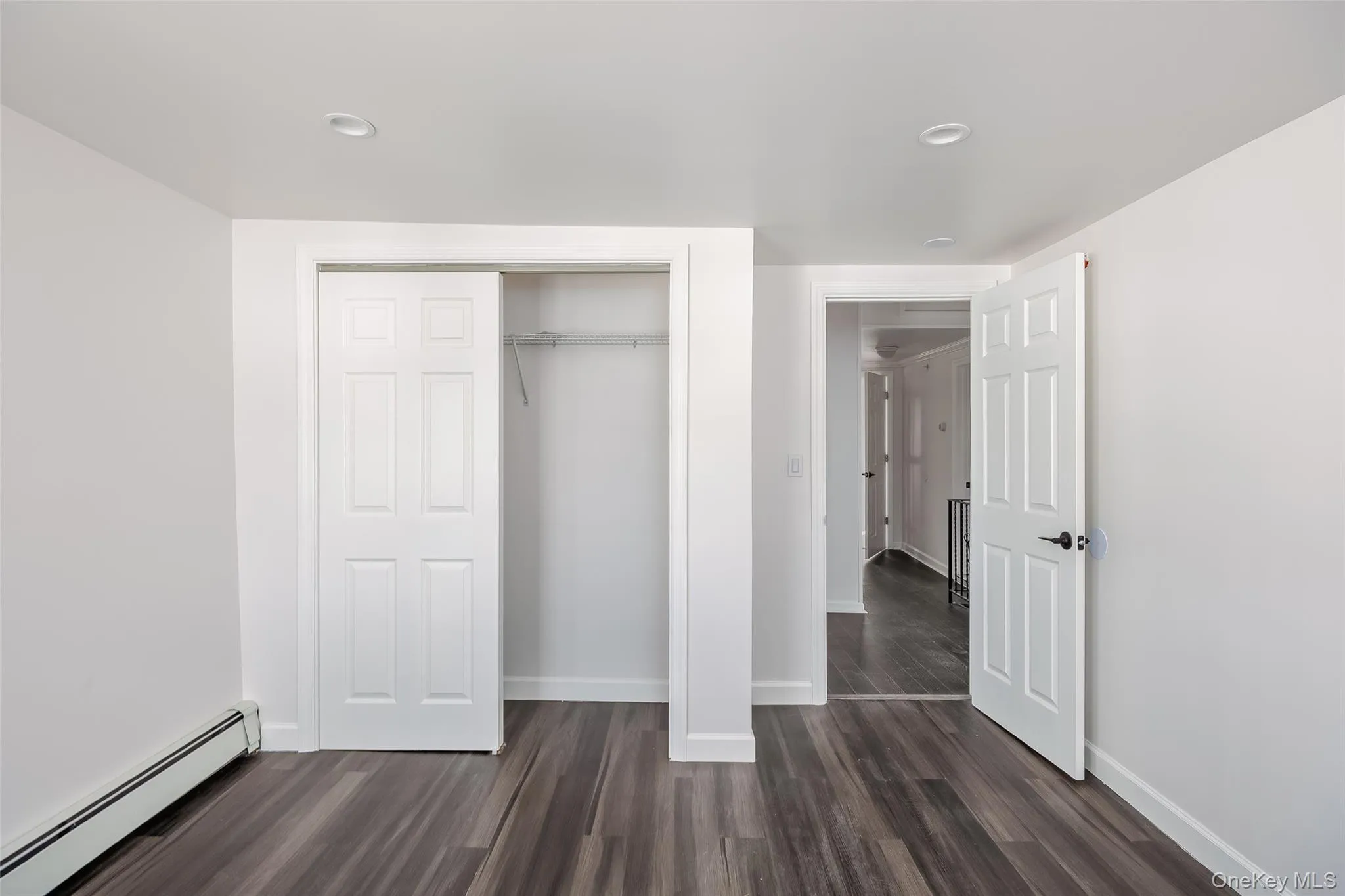 Unfurnished bedroom featuring a baseboard radiator, dark wood-style flooring, a closet, and recessed lighting Unfurnished bedroom featuring a baseboard radiator, dark wood-style flooring, a closet, and recessed lighting