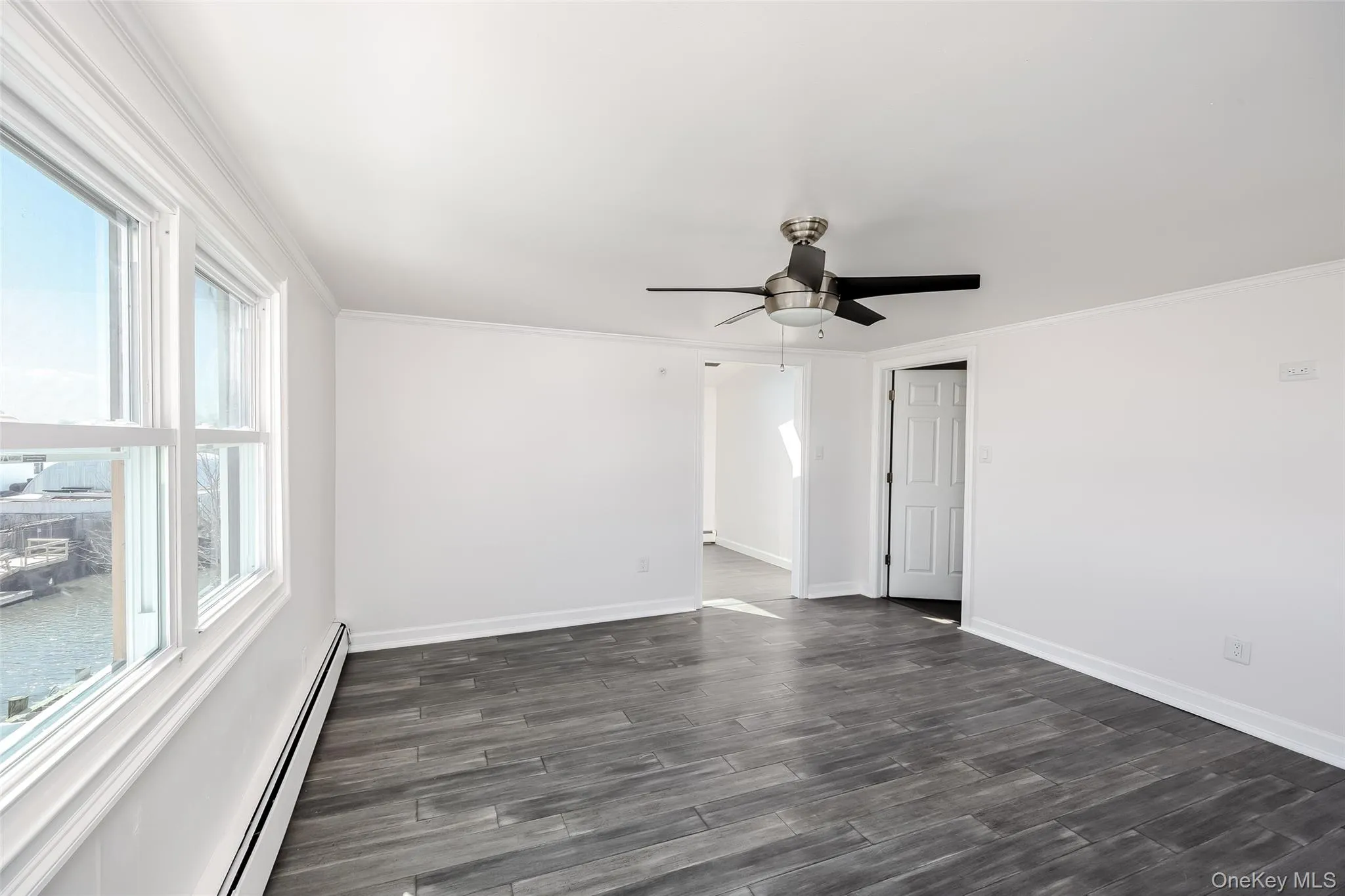 Spare room featuring a baseboard heating unit, ornamental molding, dark wood-type flooring, and a ceiling fan Spare room featuring a baseboard heating unit, ornamental molding, dark wood-type flooring, and a ceiling fan