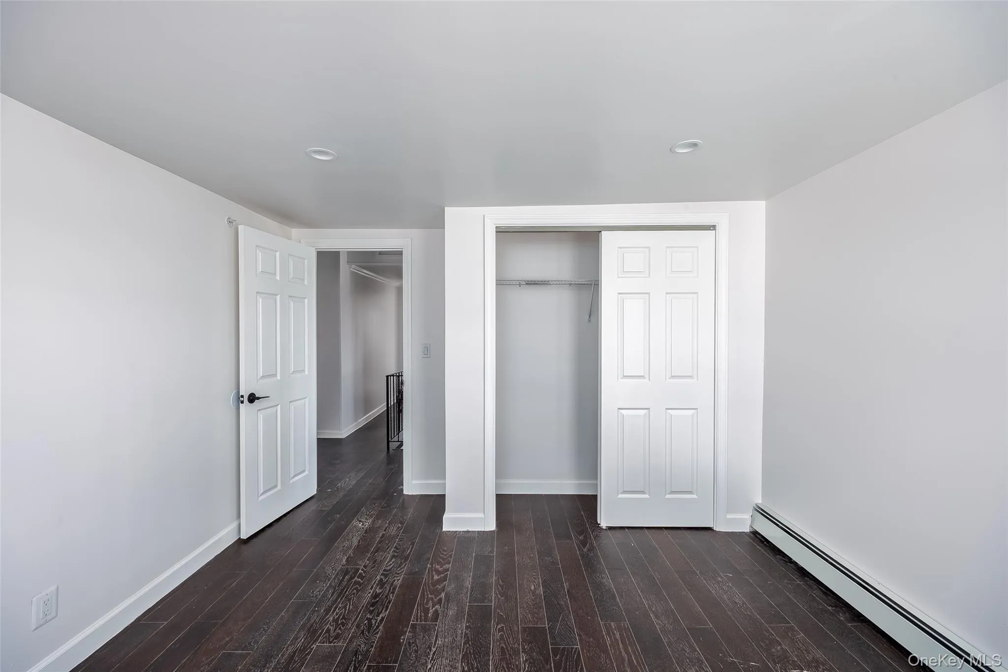 Unfurnished bedroom with a baseboard radiator, a closet, dark wood-type flooring, and recessed lighting Unfurnished bedroom with a baseboard radiator, a closet, dark wood-type flooring, and recessed lighting
