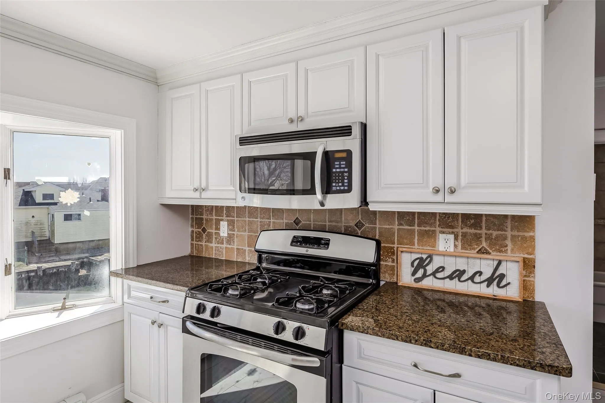 Kitchen with stainless steel appliances, white cabinets, tasteful backsplash, crown molding, and dark stone counters Kitchen with stainless steel appliances, white cabinets, tasteful backsplash, crown molding, and dark stone counters