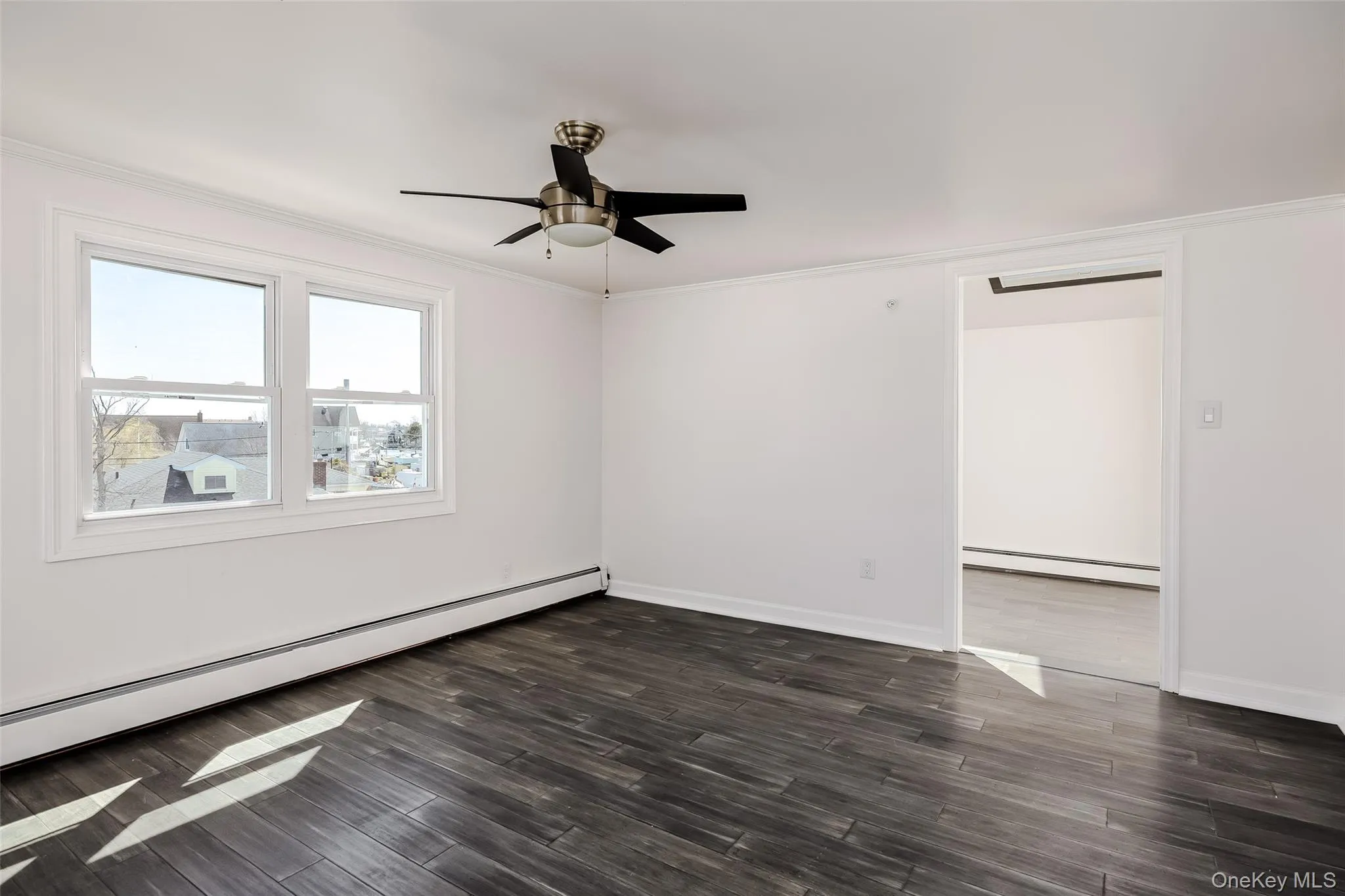Empty room with baseboard heating, ornamental molding, dark wood finished floors, and ceiling fan Empty room with baseboard heating, ornamental molding, dark wood finished floors, and ceiling fan