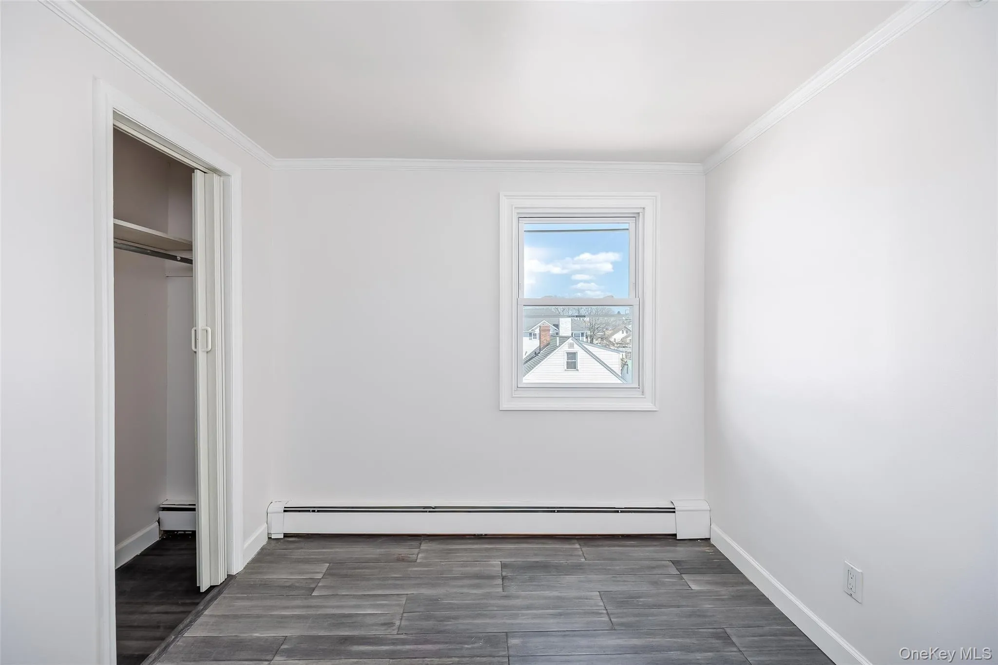 Unfurnished bedroom with a baseboard radiator, ornamental molding, a closet, and dark wood finished floors Unfurnished bedroom with a baseboard radiator, ornamental molding, a closet, and dark wood finished floors