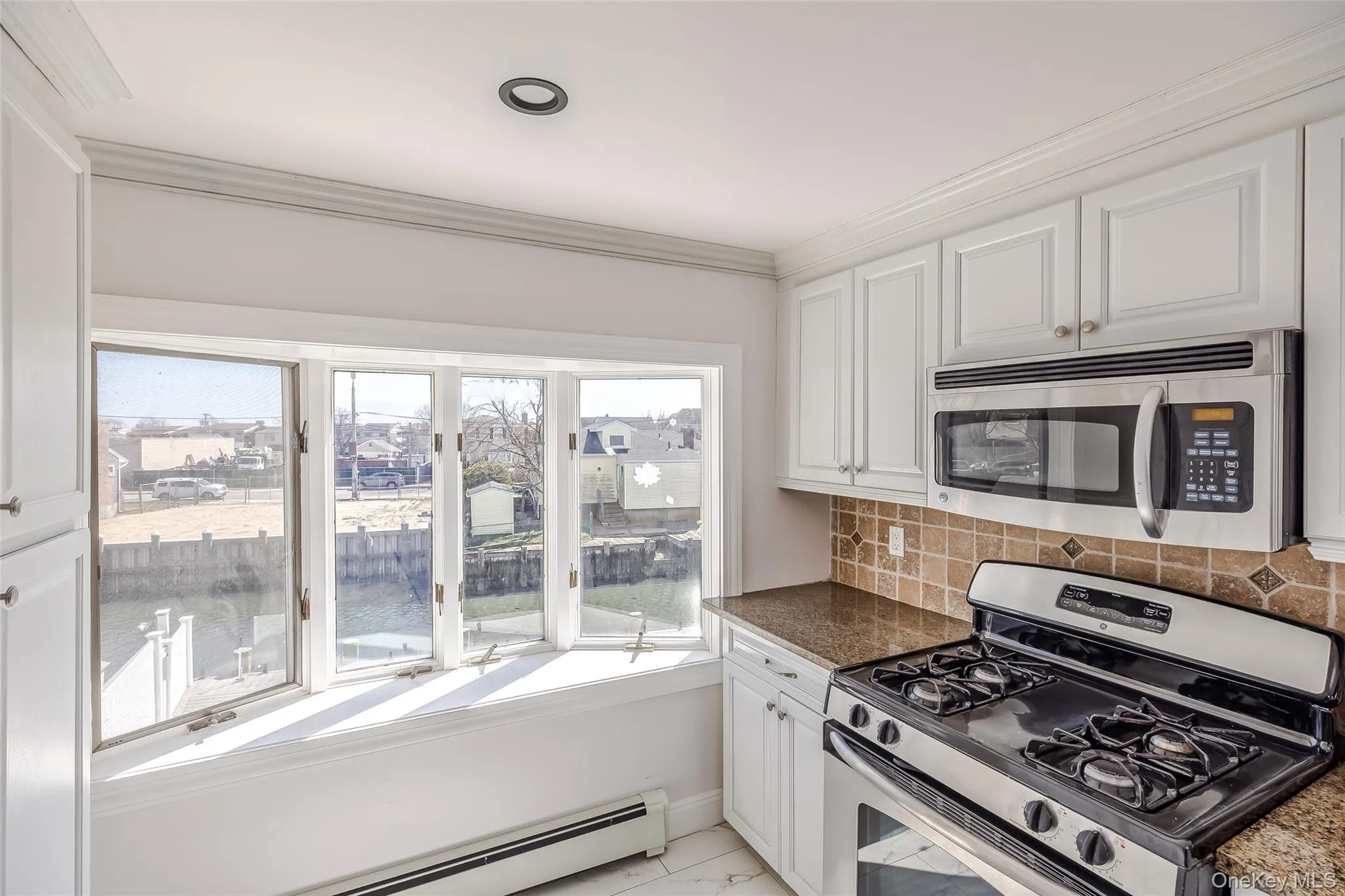 Kitchen with appliances with stainless steel finishes, white cabinets, a water view, a baseboard heating unit, and ornamental molding Kitchen with appliances with stainless steel finishes, white cabinets, a water view, a baseboard heating unit, and ornamental molding