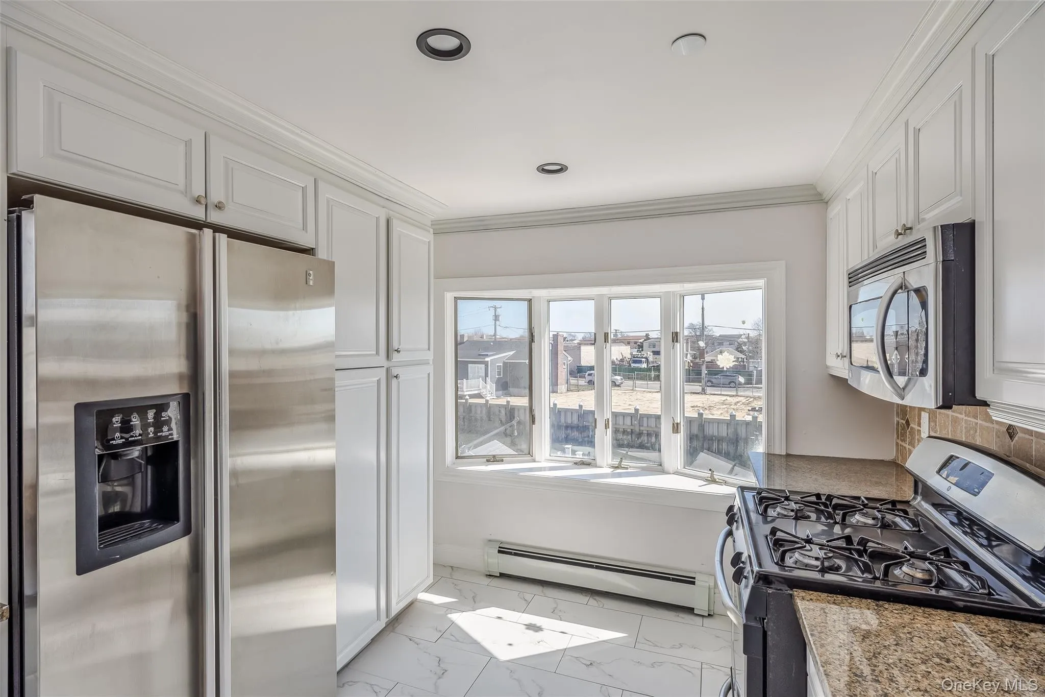 Kitchen with stainless steel appliances, a baseboard radiator, white cabinets, crown molding, and light marble finish flooring Kitchen with stainless steel appliances, a baseboard radiator, white cabinets, crown molding, and light marble finish flooring