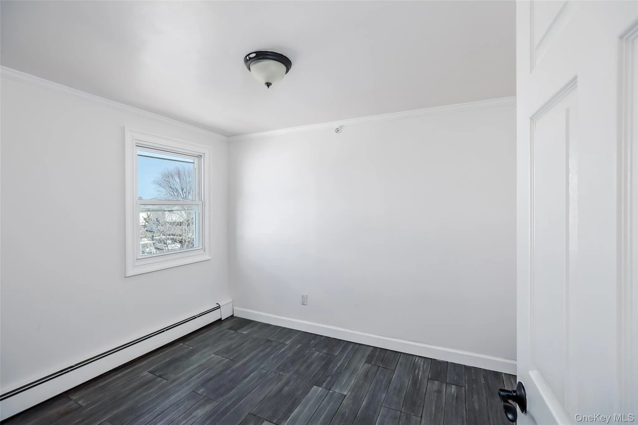 Spare room with a baseboard radiator, crown molding, and dark wood-style flooring Spare room with a baseboard radiator, crown molding, and dark wood-style flooring