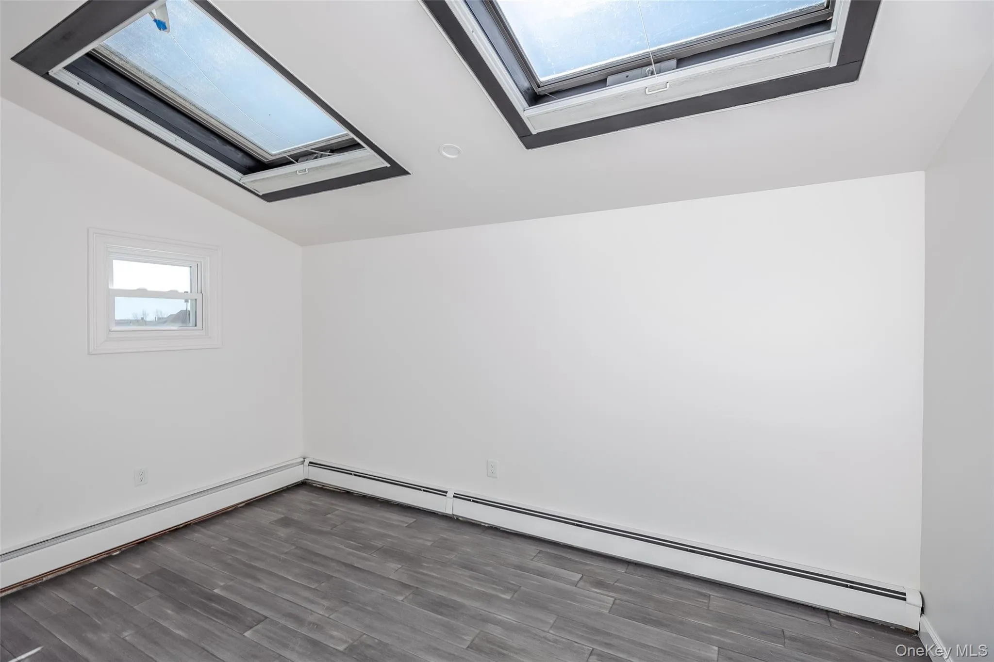 Bonus room featuring lofted ceiling, a baseboard radiator, a skylight, and wood finished floors Bonus room featuring lofted ceiling, a baseboard radiator, a skylight, and wood finished floors