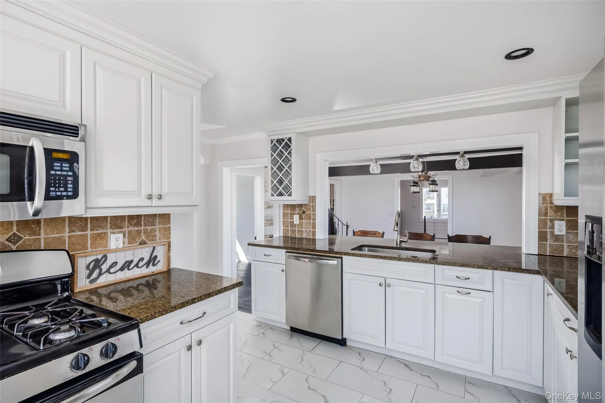 Kitchen featuring stainless steel appliances, backsplash, white cabinetry, dark stone countertops, and crown molding Kitchen featuring stainless steel appliances, backsplash, white cabinetry, dark stone countertops, and crown molding