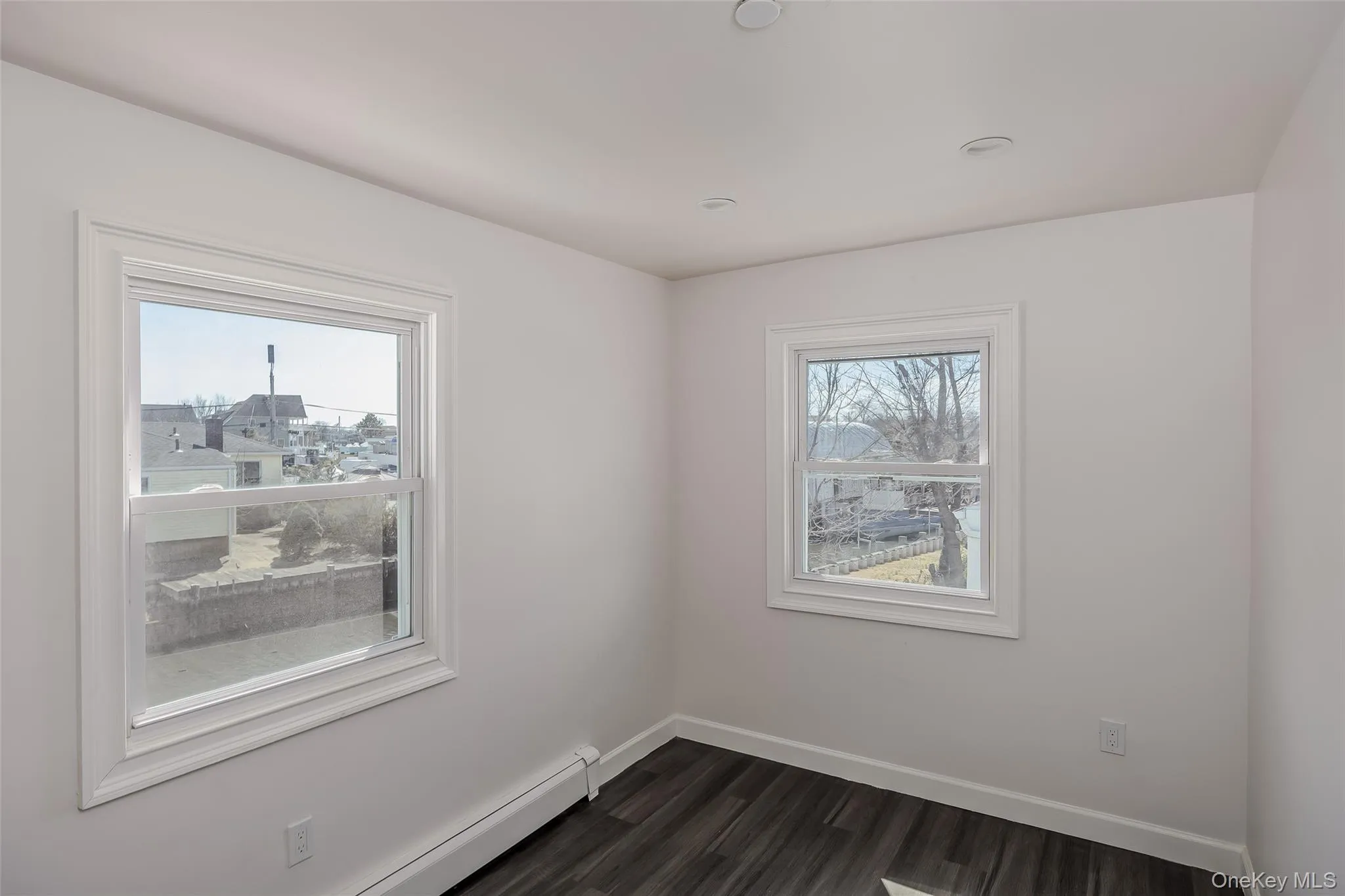 Unfurnished room with a baseboard heating unit, dark wood-style floors, and recessed lighting Unfurnished room with a baseboard heating unit, dark wood-style floors, and recessed lighting