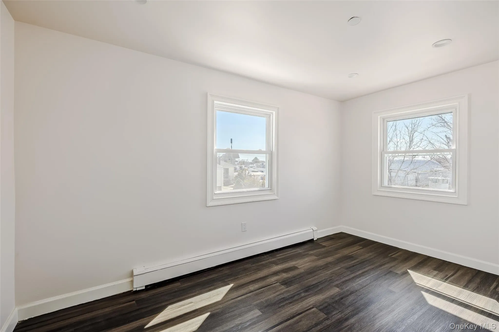 Unfurnished room featuring a baseboard heating unit and dark wood finished floors Unfurnished room featuring a baseboard heating unit and dark wood finished floors
