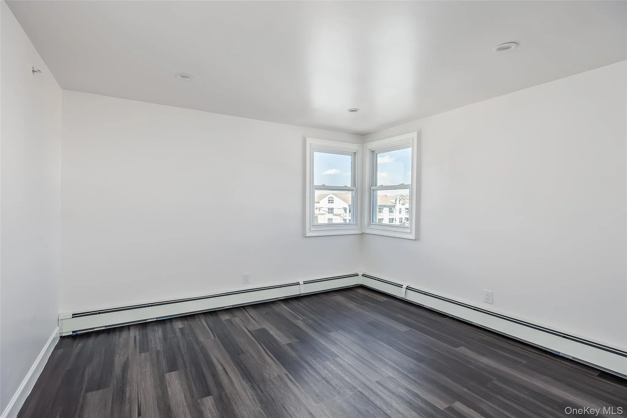Unfurnished room with dark wood-style flooring and a baseboard radiator Unfurnished room with dark wood-style flooring and a baseboard radiator