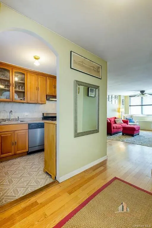Kitchen with glass insert cabinets, brown cabinetry, light wood-type flooring, and stainless steel appliances Kitchen with glass insert cabinets, brown cabinetry, light wood-type flooring, and stainless steel appliances