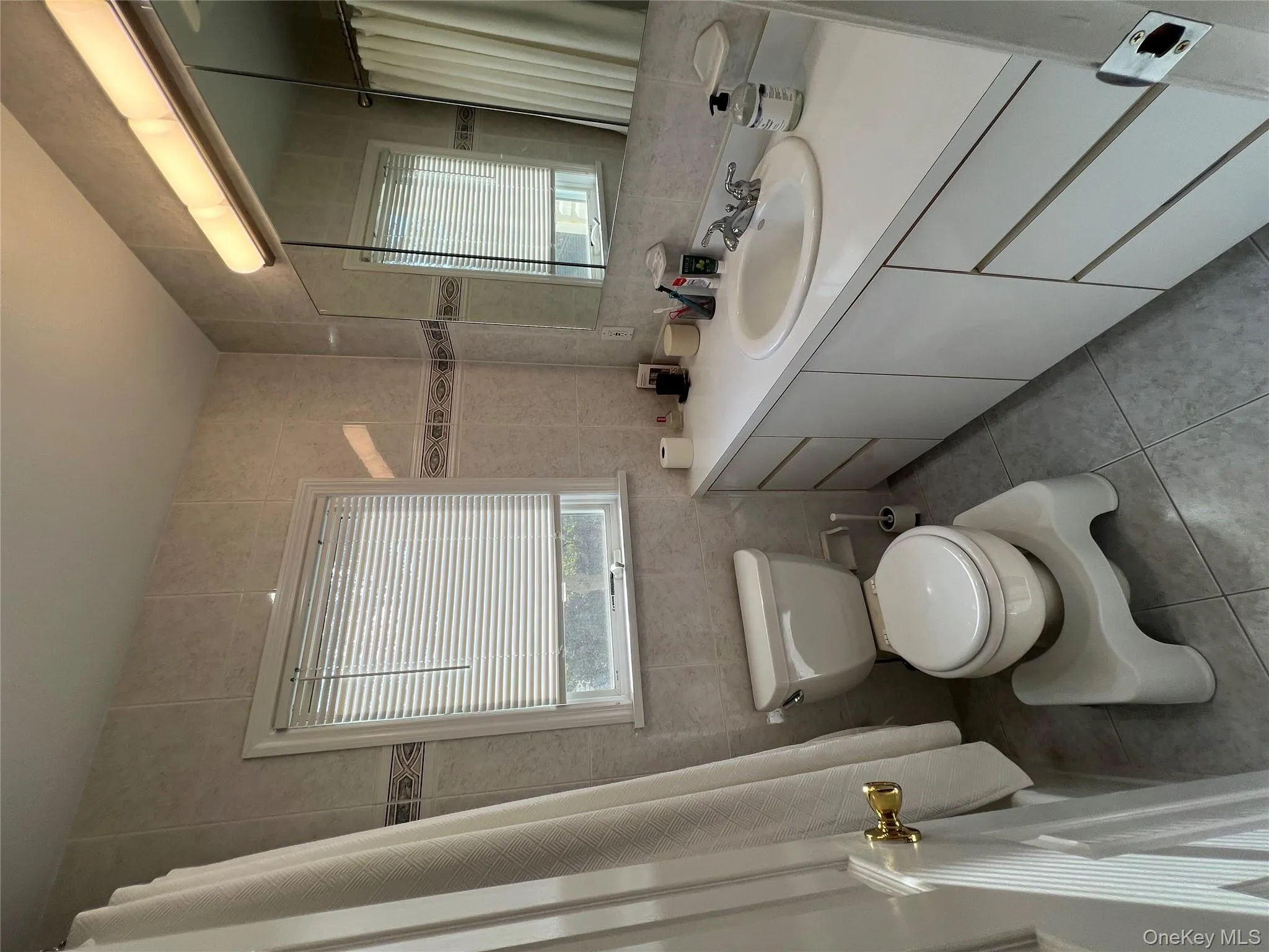 Full bathroom featuring tile walls, a shower with curtain, vanity, light tile patterned floors, and healthy amount of natural light Full bathroom featuring tile walls, a shower with curtain, vanity, light tile patterned floors, and healthy amount of natural light