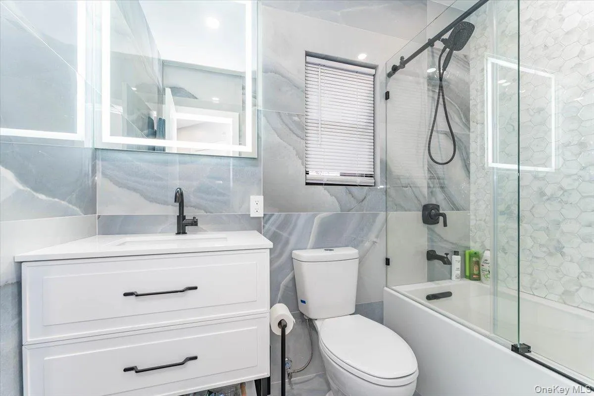 Full bath with tile walls, combined bath / shower with glass door, vanity, and backsplash Full bath with tile walls, combined bath / shower with glass door, vanity, and backsplash
