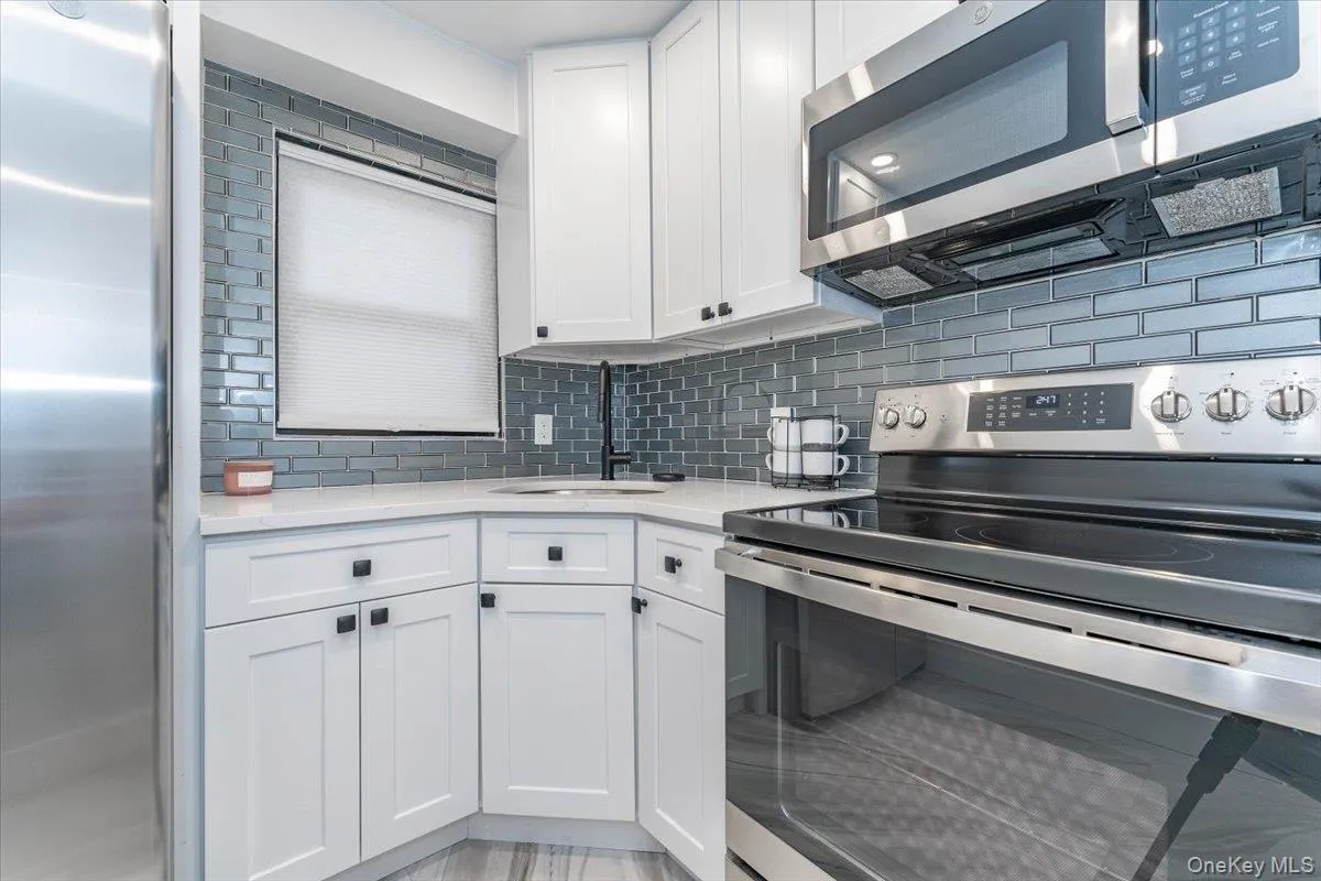 Kitchen featuring stainless steel appliances, light stone counters, backsplash, and white cabinets Kitchen featuring stainless steel appliances, light stone counters, backsplash, and white cabinets