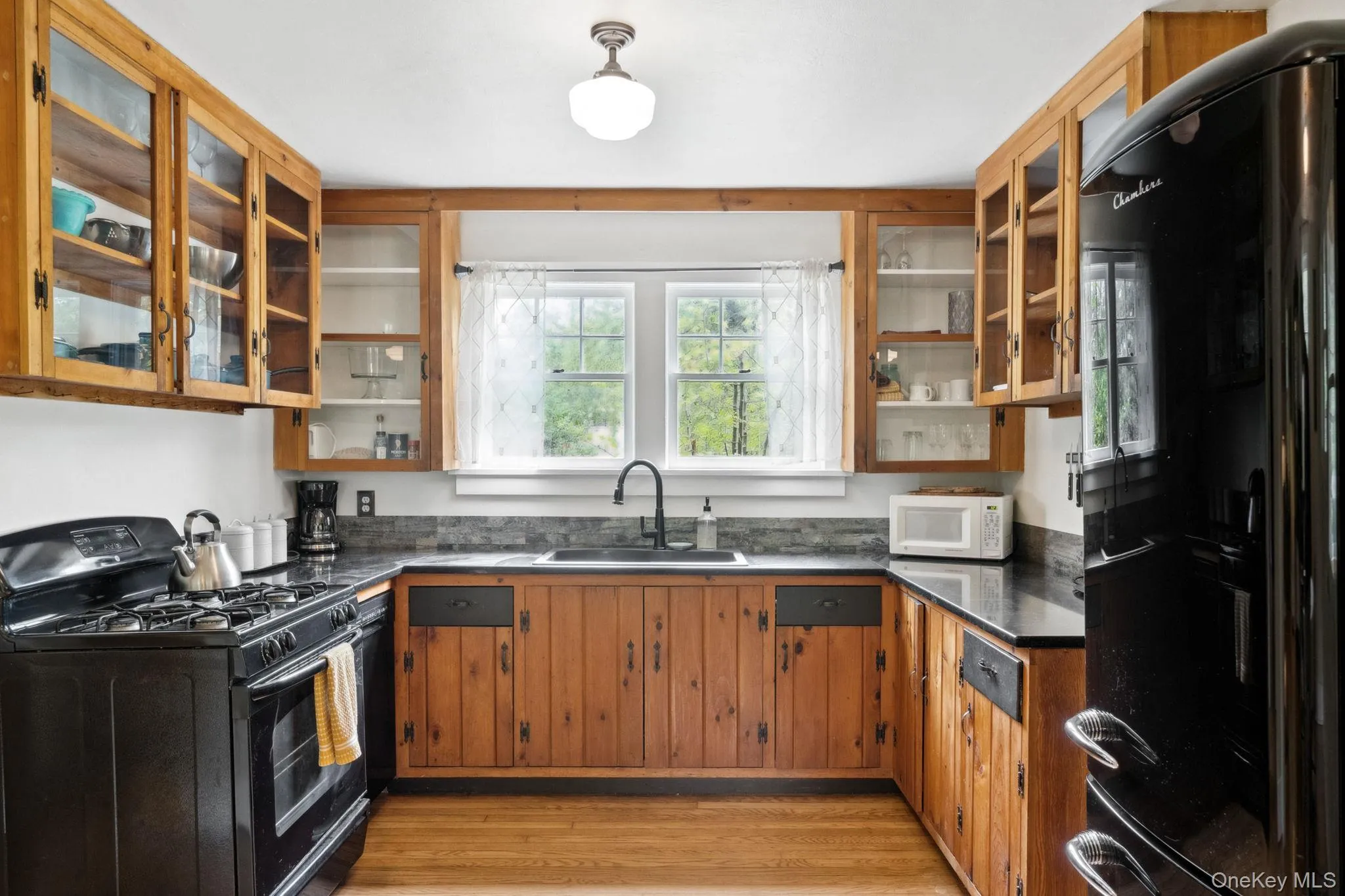 Kitchen featuring glass insert cabinets, black appliances, brown cabinets, light wood-style flooring, and open shelves Kitchen featuring glass insert cabinets, black appliances, brown cabinets, light wood-style flooring, and open shelves
