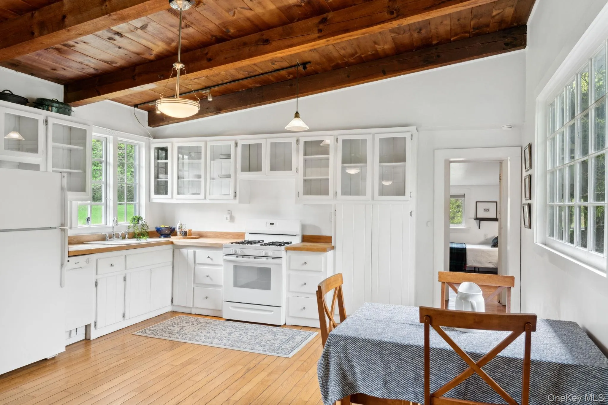 Kitchen featuring white cabinetry, white appliances, glass insert cabinets, pendant lighting, and wooden ceiling Kitchen featuring white cabinetry, white appliances, glass insert cabinets, pendant lighting, and wooden ceiling