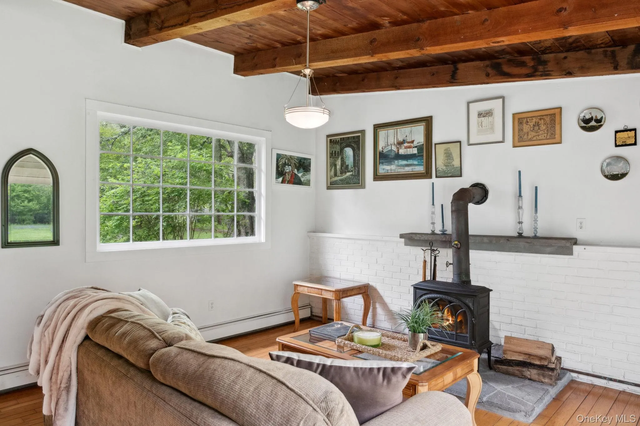 Living room with a wood stove, a wooden ceiling with exposed beams, hardwood / wood-style floors, and baseboard heating Living room with a wood stove, a wooden ceiling with exposed beams, hardwood / wood-style floors, and baseboard heating
