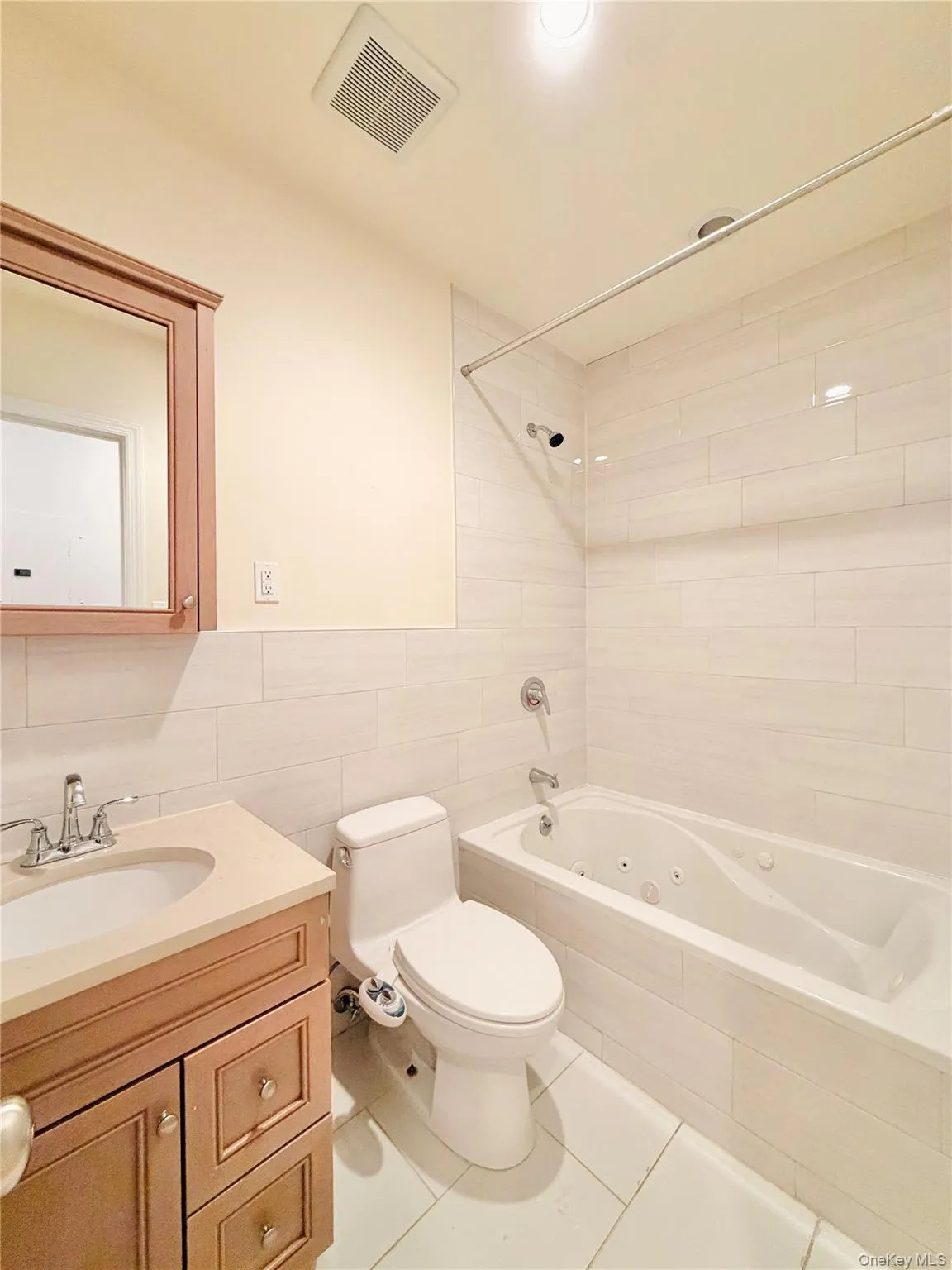 Bathroom featuring tile walls, vanity, light tile patterned floors, a combined bath / shower with jetted tub, and recessed lighting Bathroom featuring tile walls, vanity, light tile patterned floors, a combined bath / shower with jetted tub, and recessed lighting