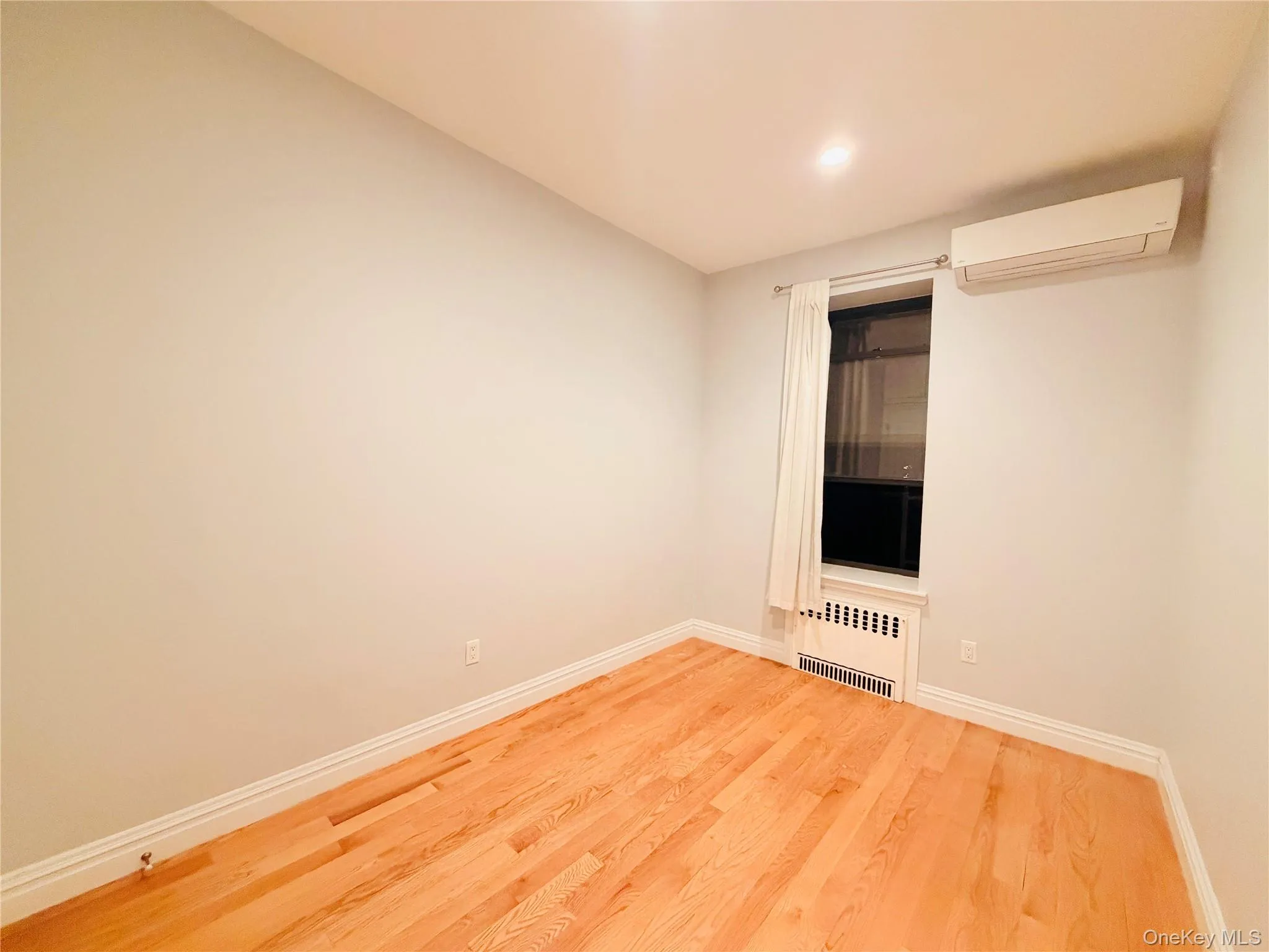 Unfurnished room with wood finished floors, an AC wall unit, and radiator heating unit Unfurnished room with wood finished floors, an AC wall unit, and radiator heating unit