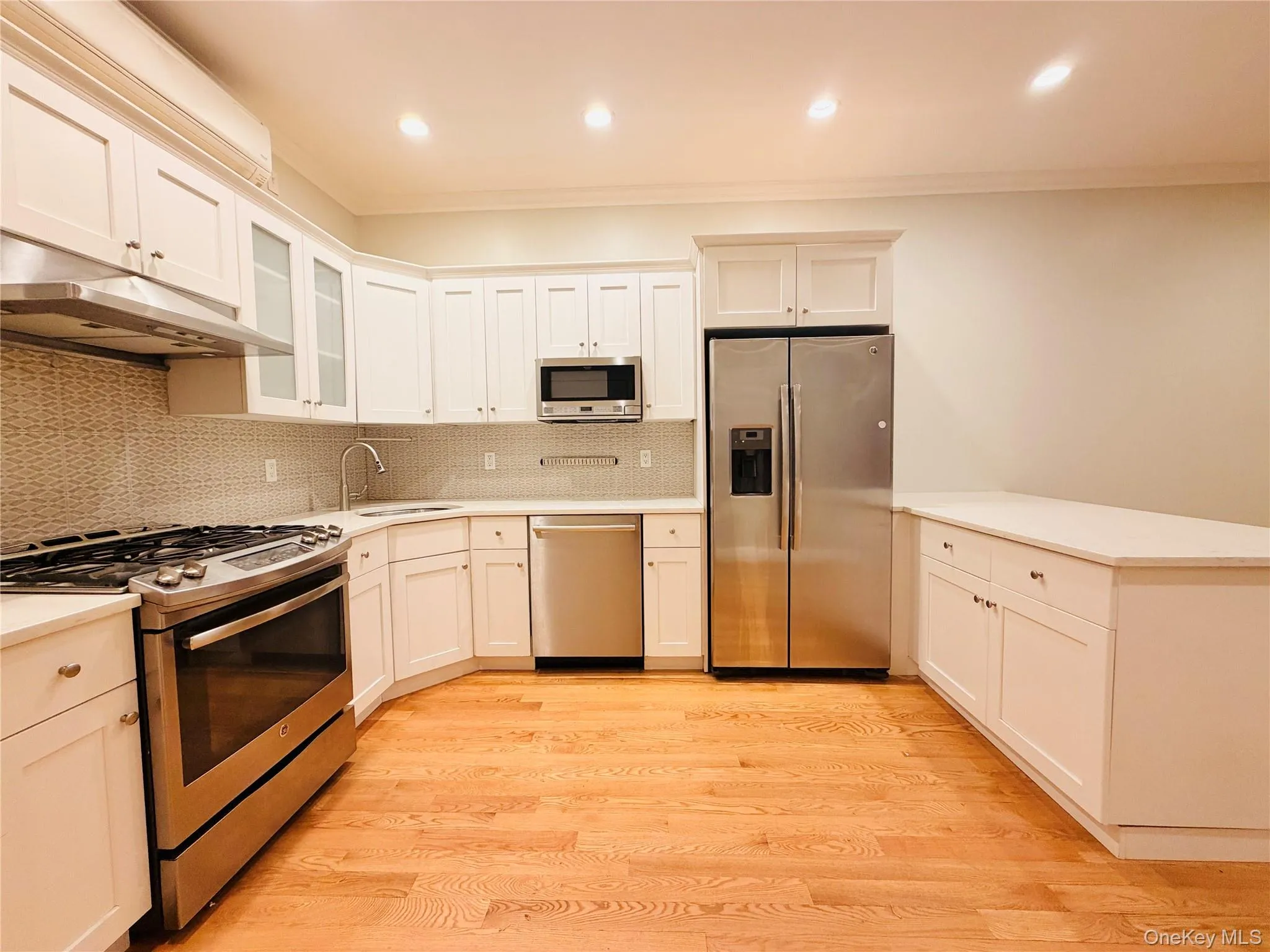 Kitchen featuring stainless steel appliances, light wood-style flooring, recessed lighting, decorative backsplash, and glass insert cabinets Kitchen featuring stainless steel appliances, light wood-style flooring, recessed lighting, decorative backsplash, and glass insert cabinets