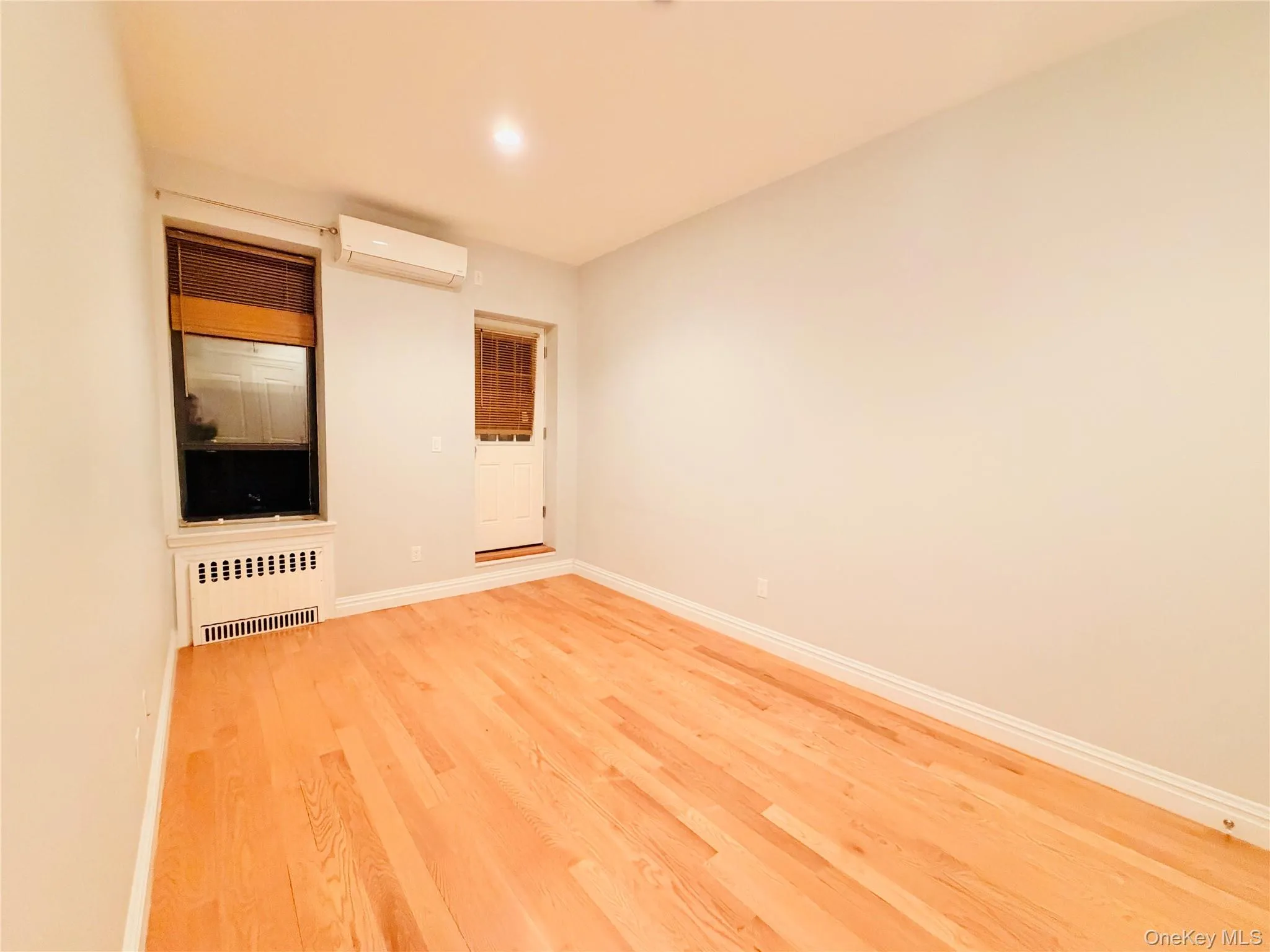 Spare room with radiator, wood finished floors, and a wall mounted air conditioner Spare room with radiator, wood finished floors, and a wall mounted air conditioner