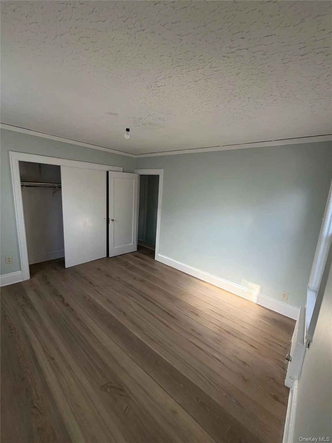 Unfurnished bedroom with wood finished floors, a textured ceiling, crown molding, and a closet Unfurnished bedroom with wood finished floors, a textured ceiling, crown molding, and a closet