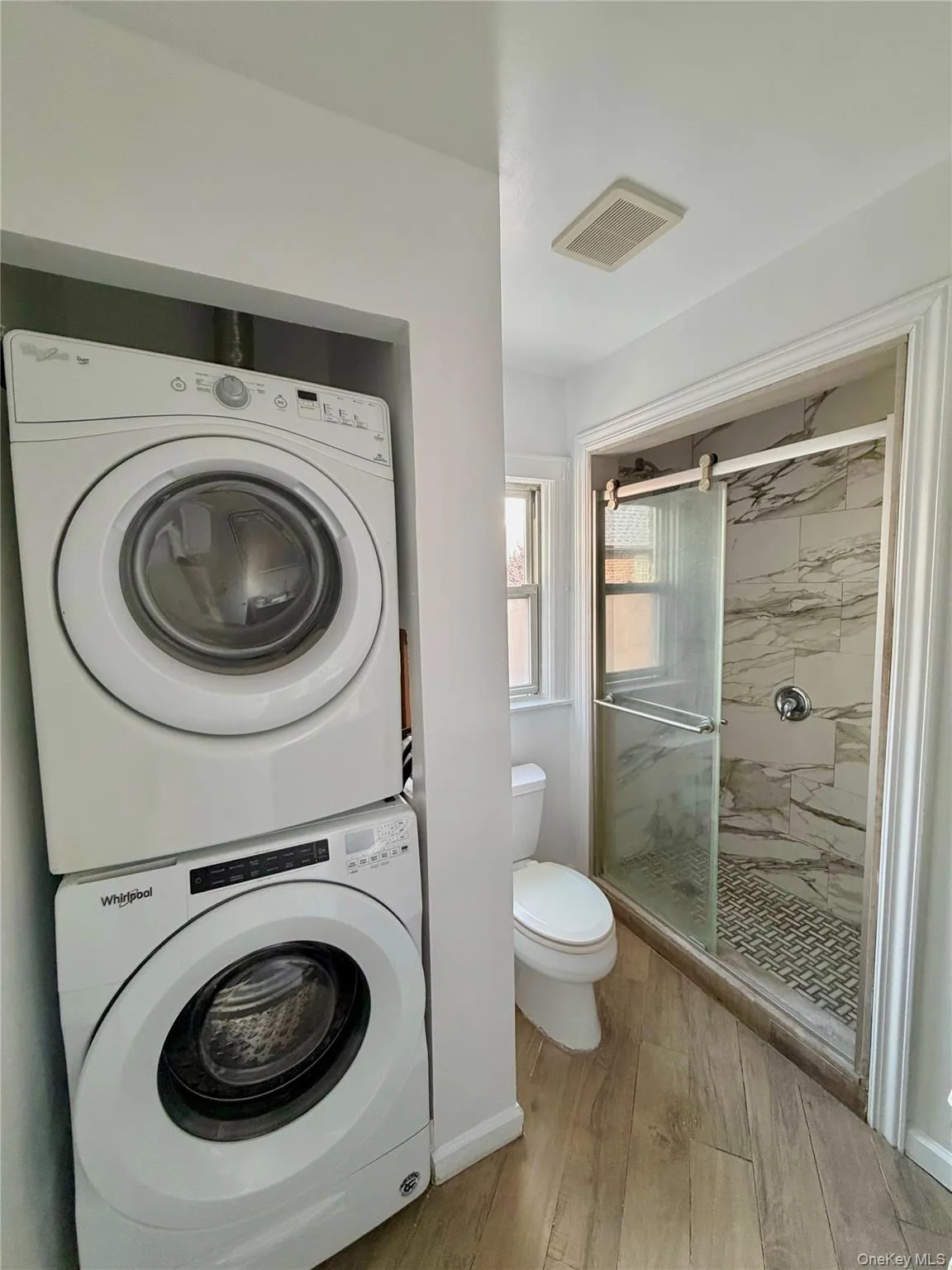 Laundry area featuring light wood-style flooring and stacked washing machine and dryer Laundry area featuring light wood-style flooring and stacked washing machine and dryer