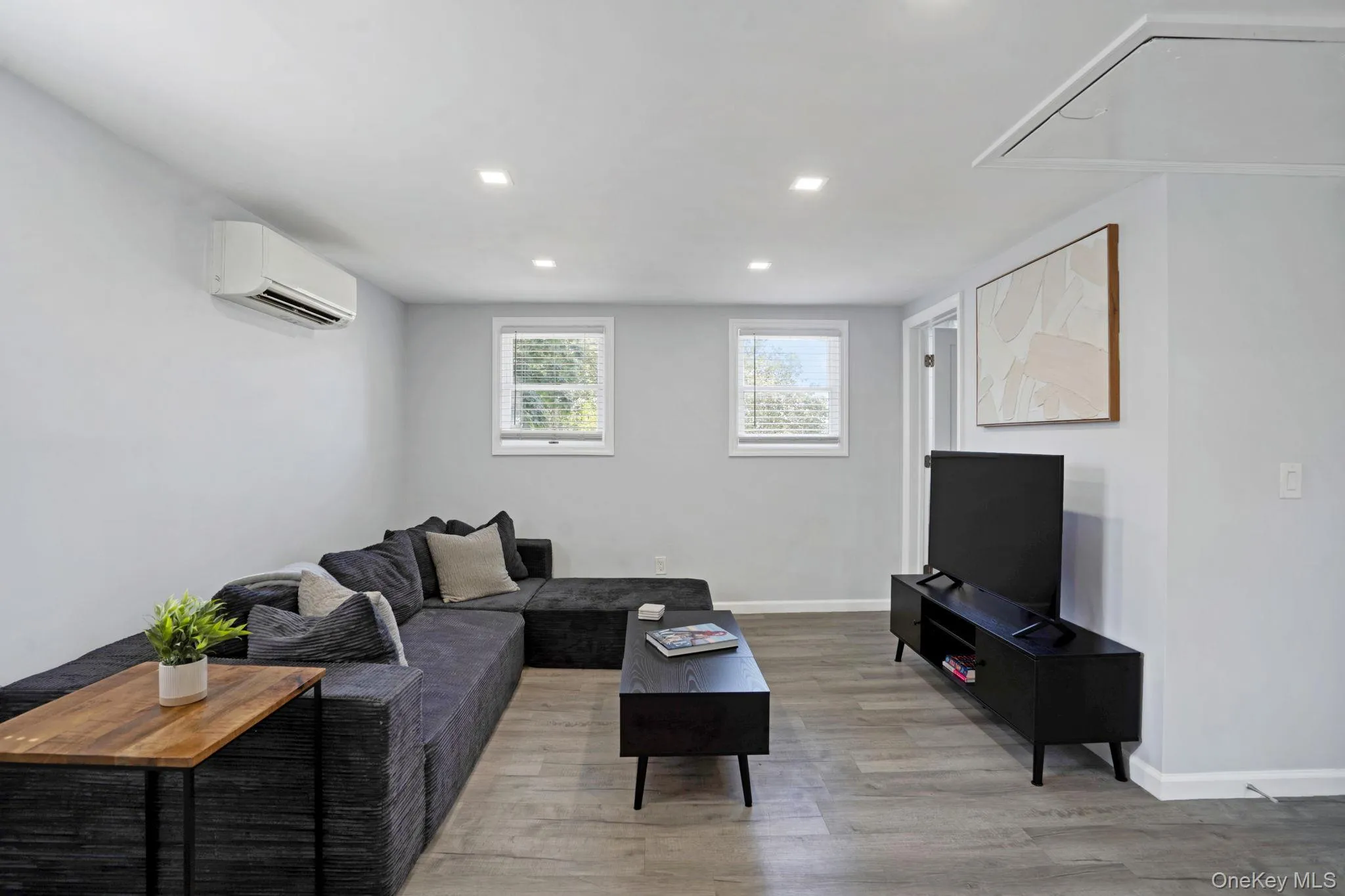 Living room featuring light wood-style flooring, recessed lighting, and a wall mounted air conditioner Living room featuring light wood-style flooring, recessed lighting, and a wall mounted air conditioner