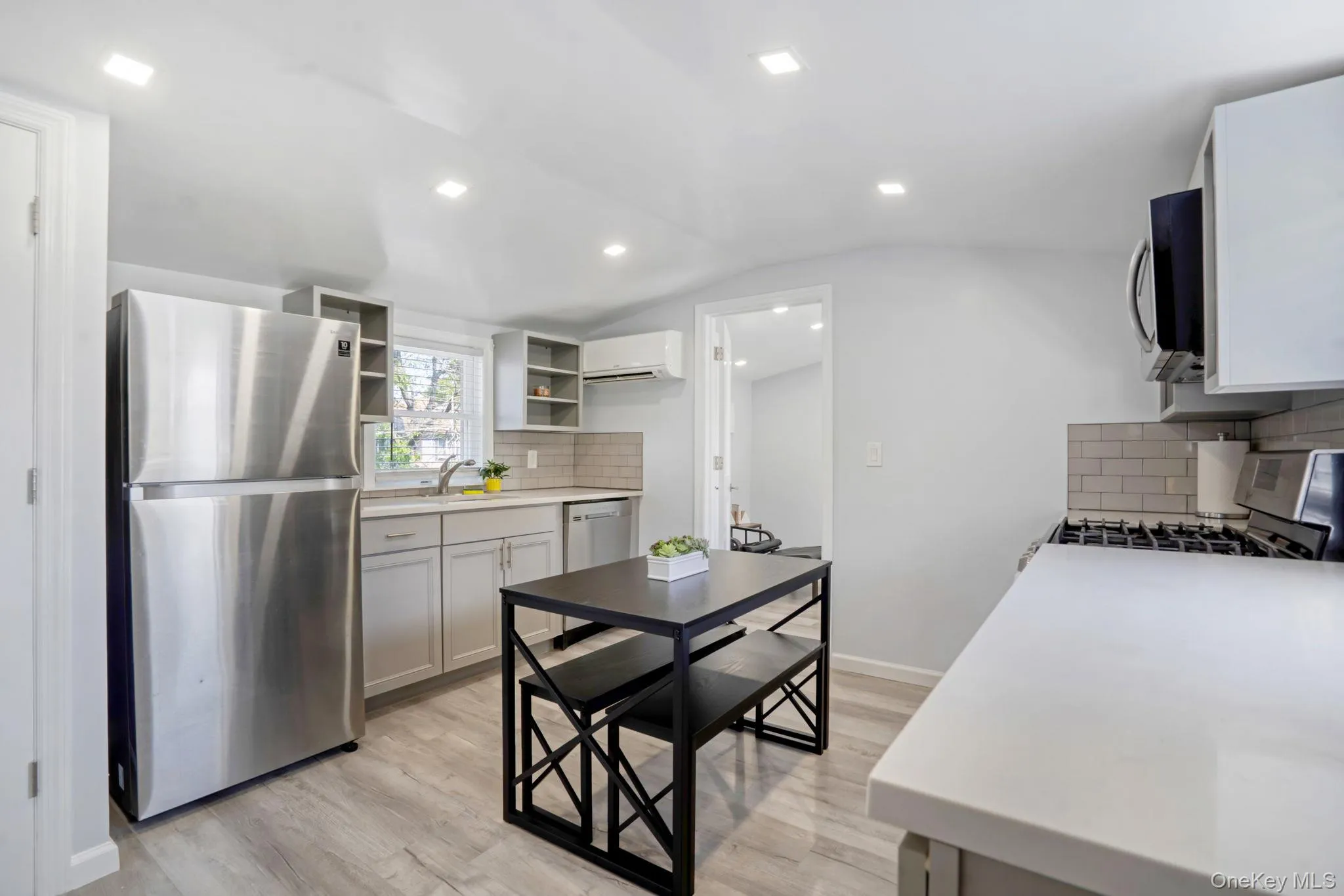 Kitchen with decorative backsplash, appliances with stainless steel finishes, gray cabinets, light wood-type flooring, and lofted ceiling Kitchen with decorative backsplash, appliances with stainless steel finishes, gray cabinets, light wood-type flooring, and lofted ceiling
