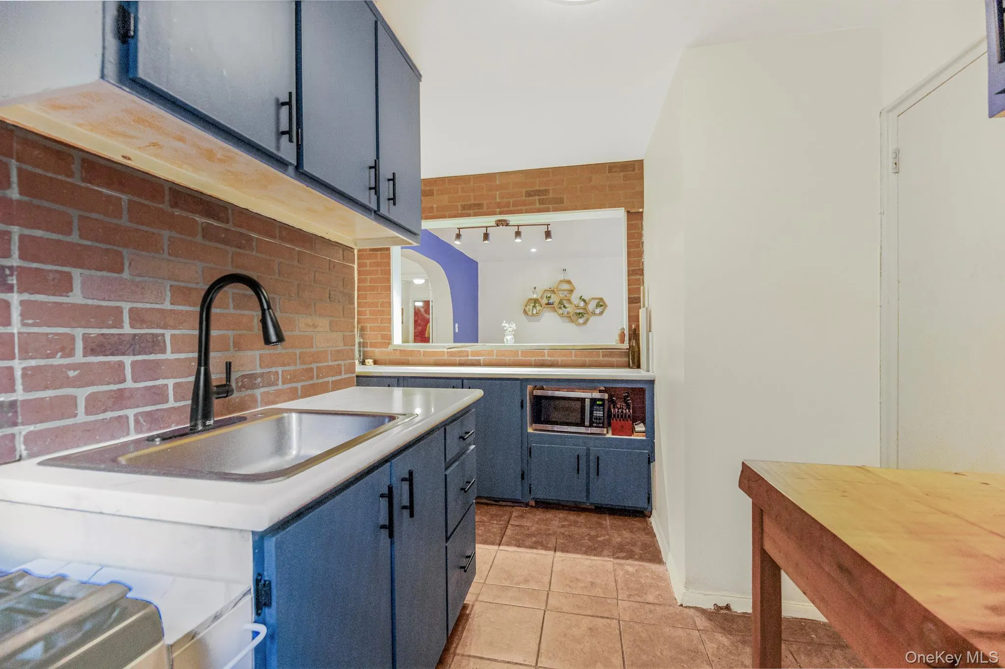 Kitchen featuring light tile patterned floors, light countertops, blue cabinetry, tasteful backsplash, and brick wall Kitchen featuring light tile patterned floors, light countertops, blue cabinetry, tasteful backsplash, and brick wall