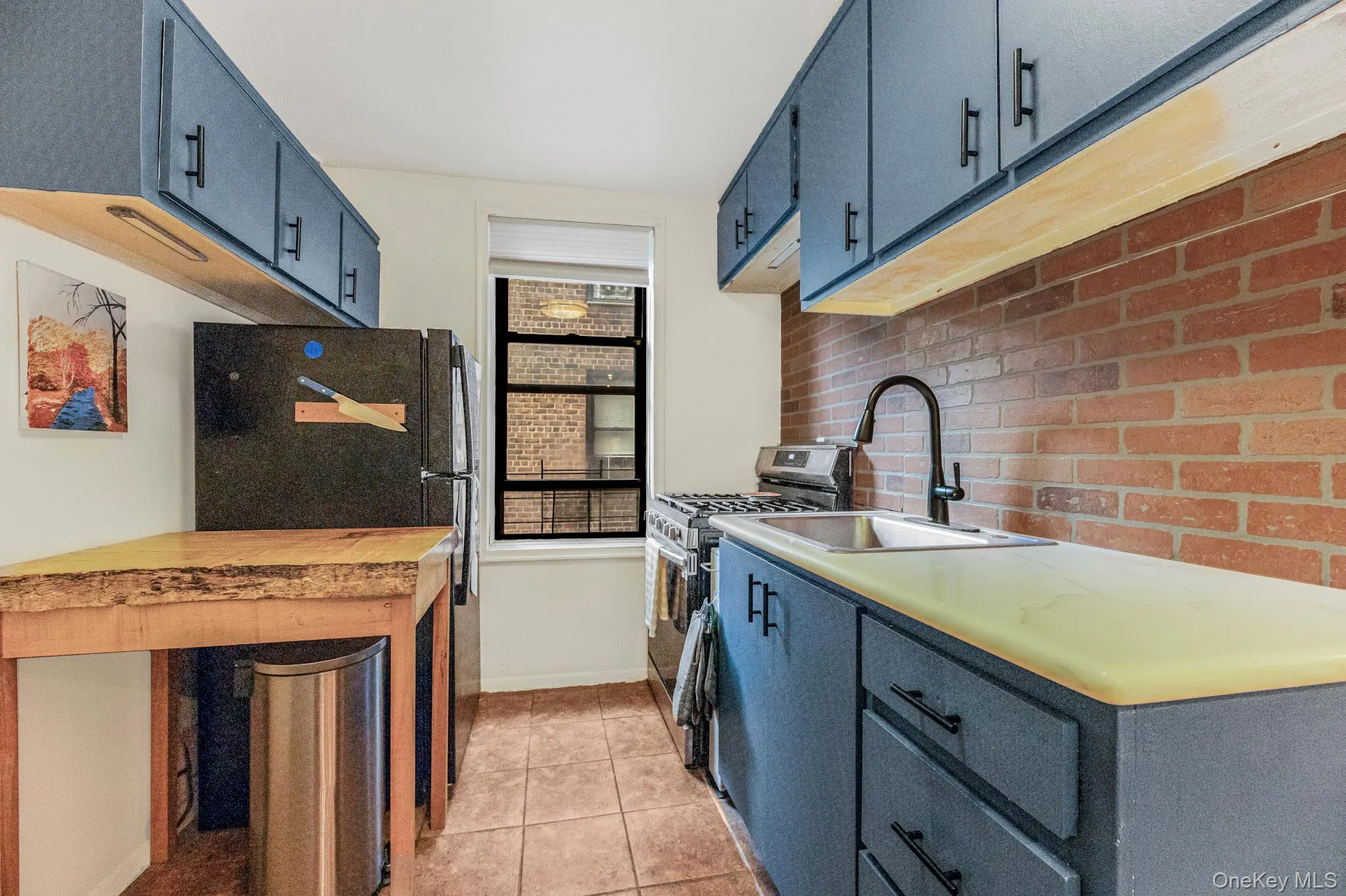 Kitchen with stainless steel gas range oven, light tile patterned floors, freestanding refrigerator, and blue cabinets Kitchen with stainless steel gas range oven, light tile patterned floors, freestanding refrigerator, and blue cabinets