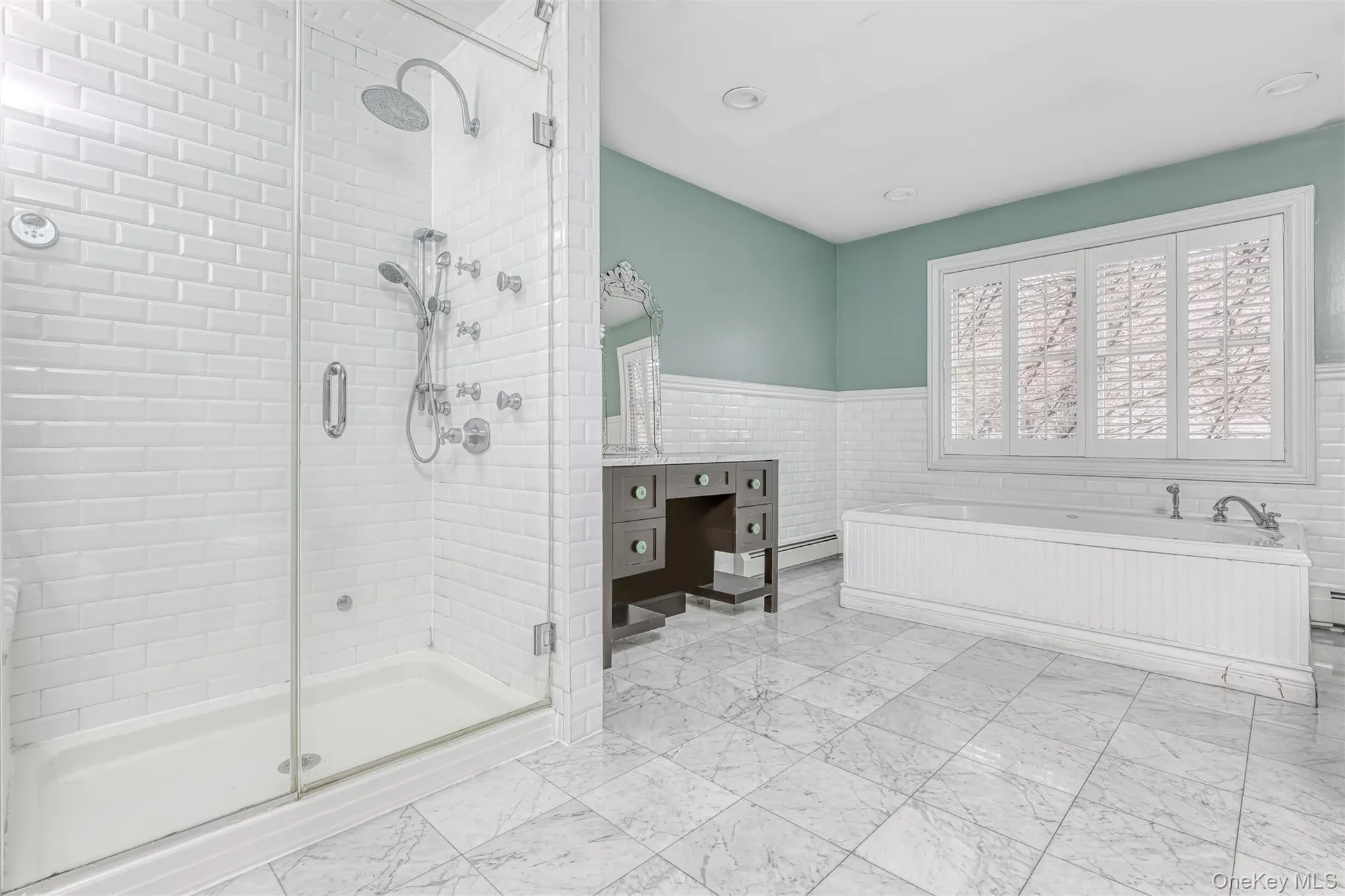 Full bath with tile walls, a stall shower, a wainscoted wall, a garden tub, and light marble finish flooring Full bath with tile walls, a stall shower, a wainscoted wall, a garden tub, and light marble finish flooring