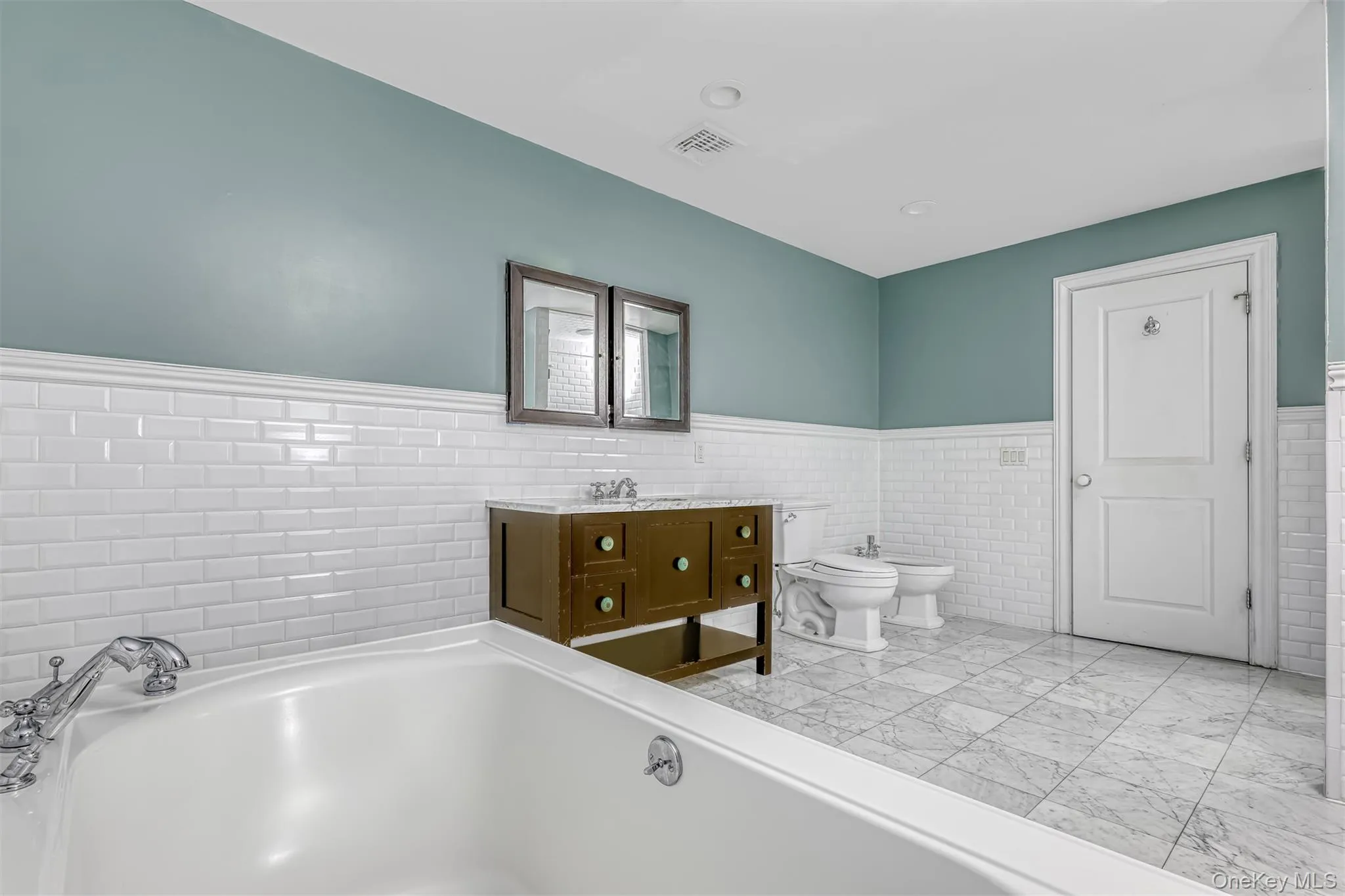 Bathroom featuring tile walls, a wainscoted wall, a bidet, vanity, and a bath Bathroom featuring tile walls, a wainscoted wall, a bidet, vanity, and a bath