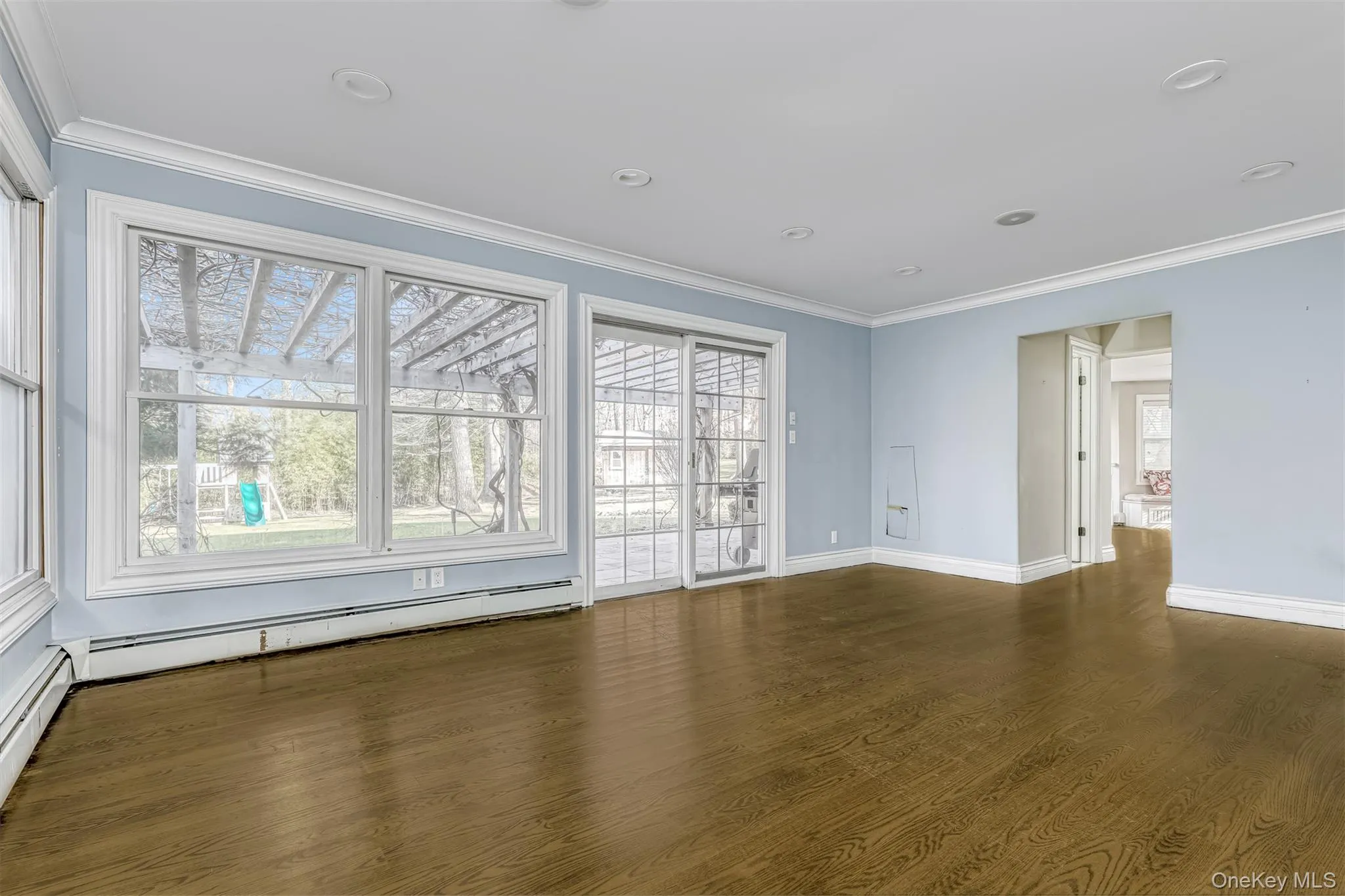 Unfurnished room featuring crown molding, dark wood finished floors, healthy amount of natural light, recessed lighting, and a baseboard heating unit Unfurnished room featuring crown molding, dark wood finished floors, healthy amount of natural light, recessed lighting, and a baseboard heating unit