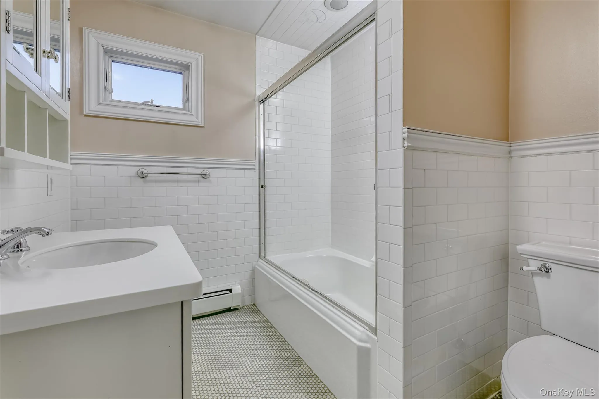 Full bath with tile walls, a wainscoted wall, vanity, a baseboard heating unit, and combined bath / shower with glass door Full bath with tile walls, a wainscoted wall, vanity, a baseboard heating unit, and combined bath / shower with glass door
