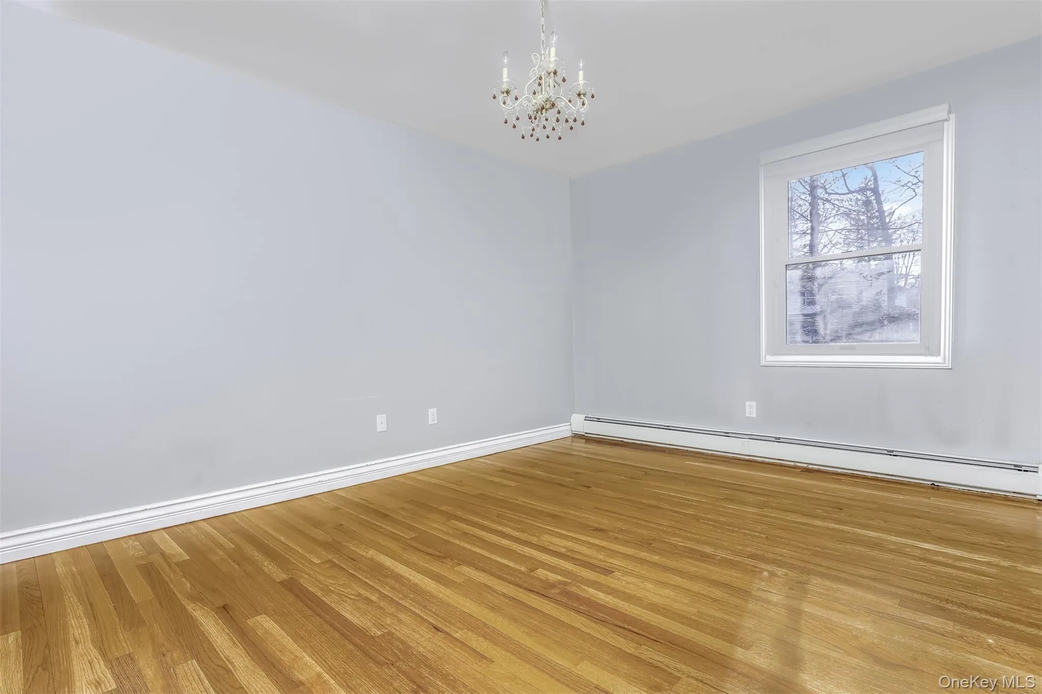 Unfurnished room featuring a baseboard radiator, a chandelier, and light wood finished floors Unfurnished room featuring a baseboard radiator, a chandelier, and light wood finished floors