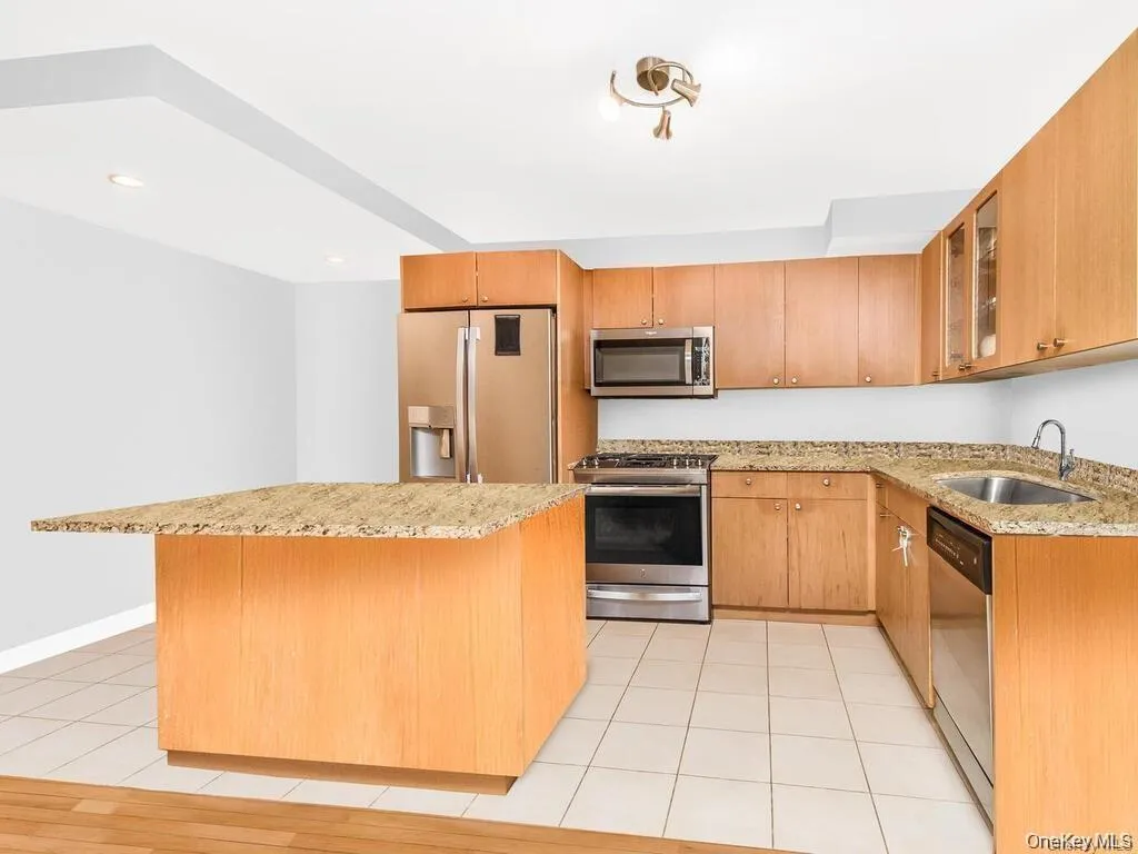 Kitchen with stainless steel appliances, light stone counters, glass insert cabinets, light tile patterned floors, and a kitchen island Kitchen with stainless steel appliances, light stone counters, glass insert cabinets, light tile patterned floors, and a kitchen island