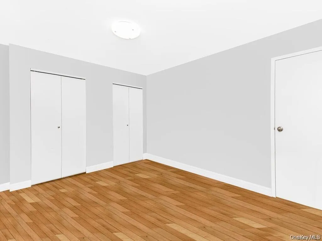 Unfurnished bedroom with multiple closets and hardwood / wood-style flooring Unfurnished bedroom with multiple closets and hardwood / wood-style flooring