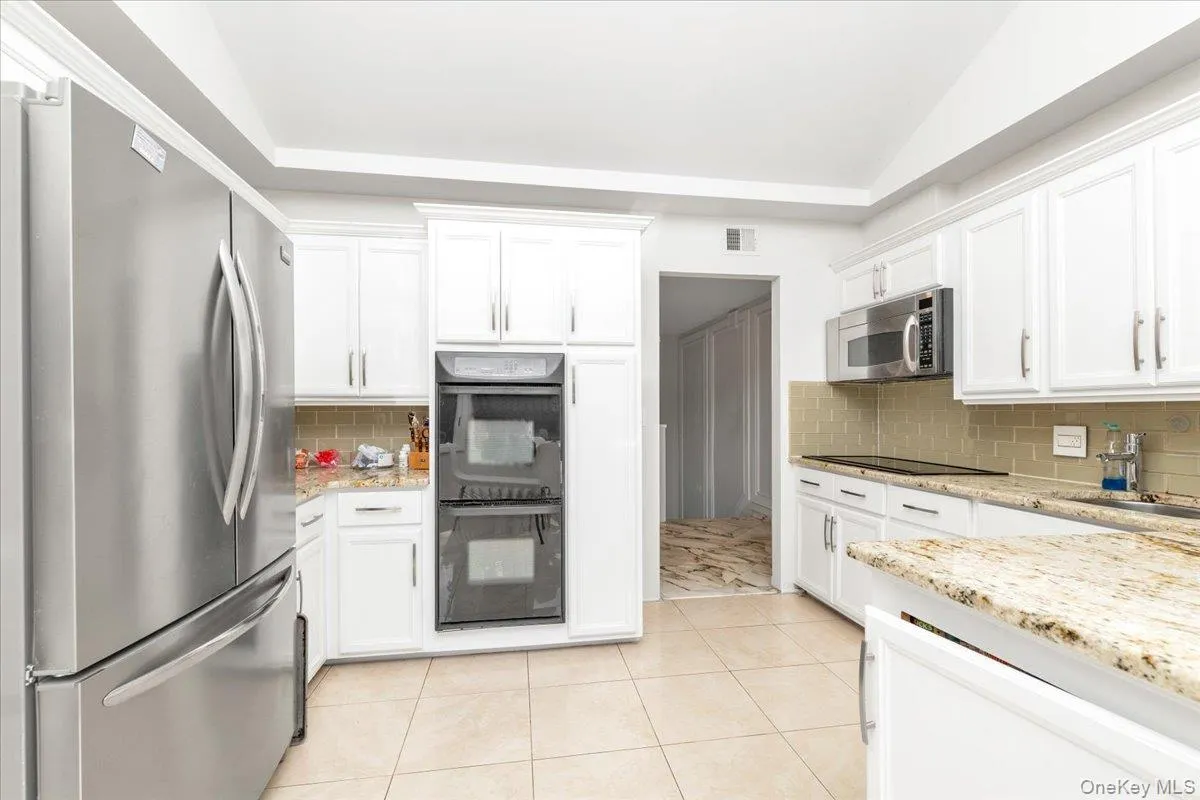 Kitchen with black appliances, white cabinets, light tile patterned flooring, light stone countertops, and vaulted ceiling Kitchen with black appliances, white cabinets, light tile patterned flooring, light stone countertops, and vaulted ceiling